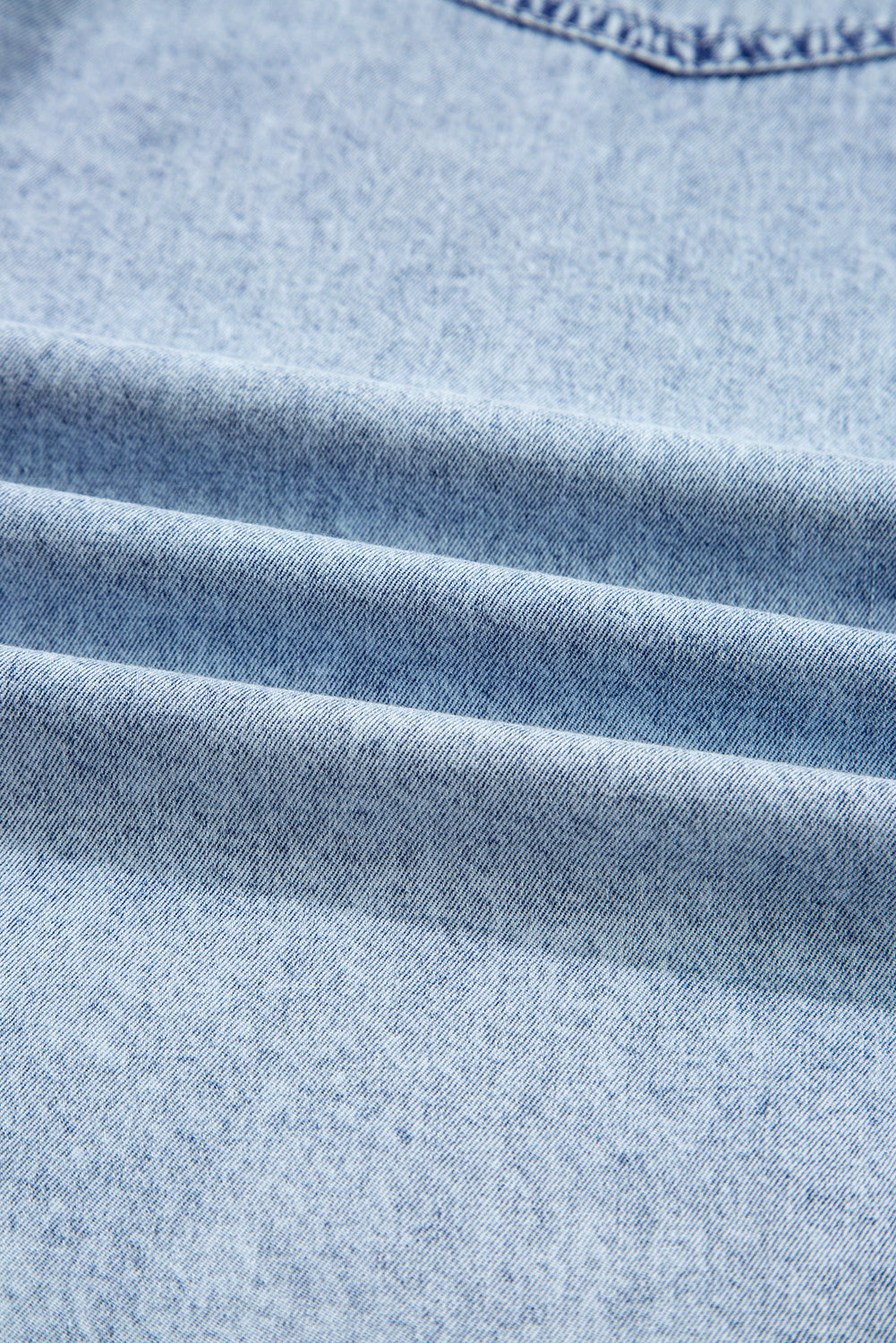 Close-up of light blue denim fabric with textured weave and stitched seam detail