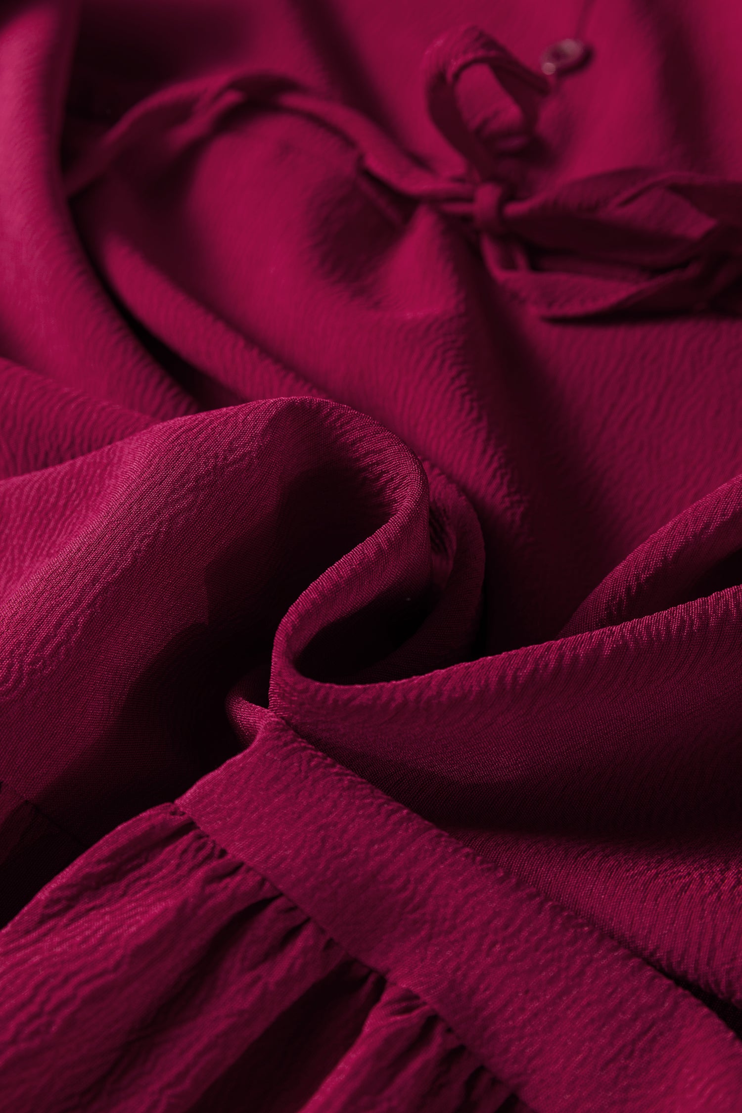 Close-up of textured burgundy fabric with gathered detail and tie, elegant textile material