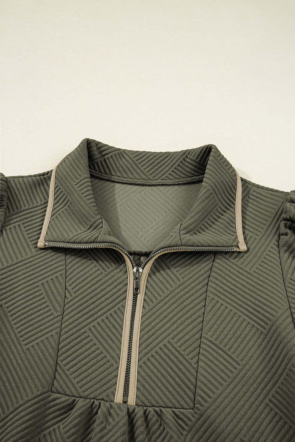 Close-up of quilted olive green jacket with geometric pattern and front half zipper