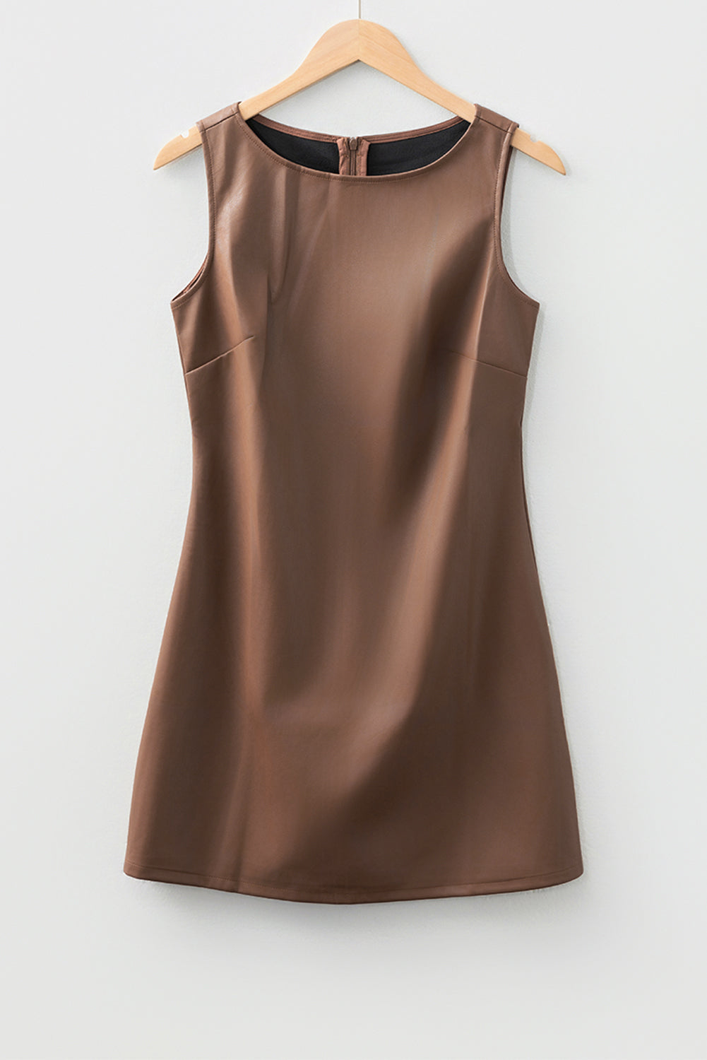Sleeveless brown faux leather mini dress on wooden hanger against white wall