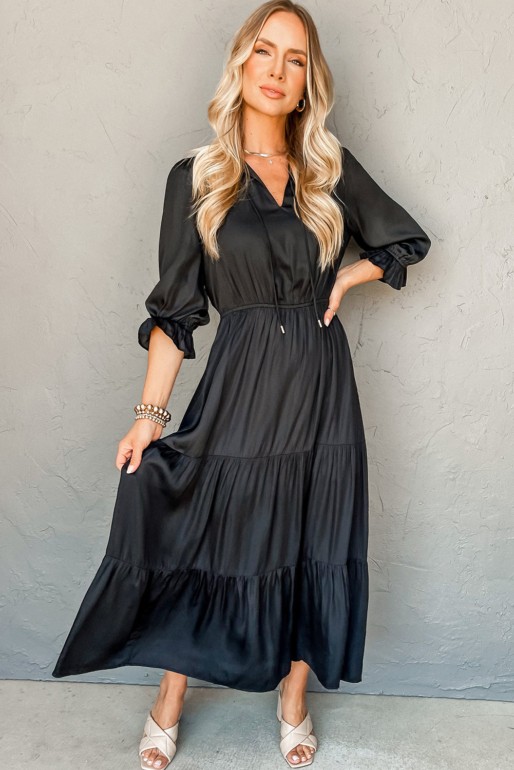 Woman wearing a black long-sleeve tiered midi dress with v-neck and neutral sandals