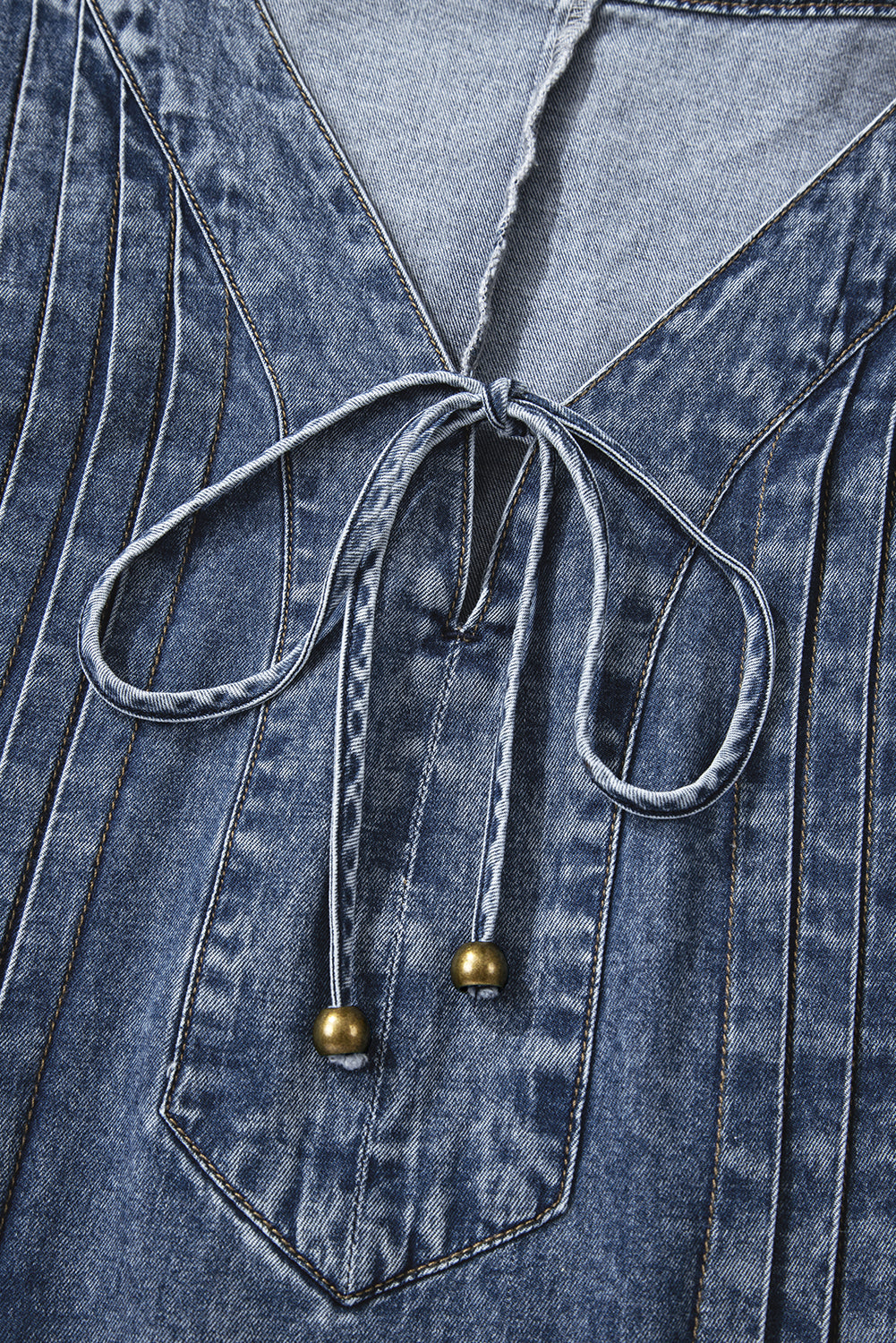 Close-up of blue denim V-neck top with stitched pleats and drawstring with metal beads