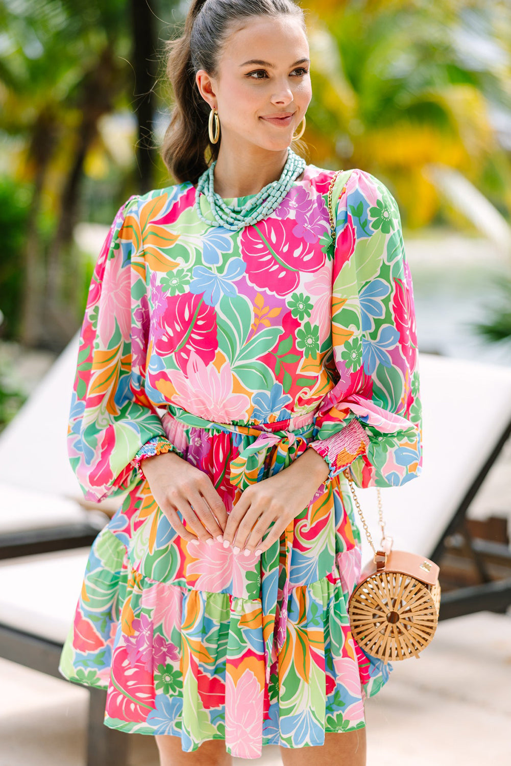 Woman in colorful floral dress with puff sleeves, wicker purse by tropical poolside