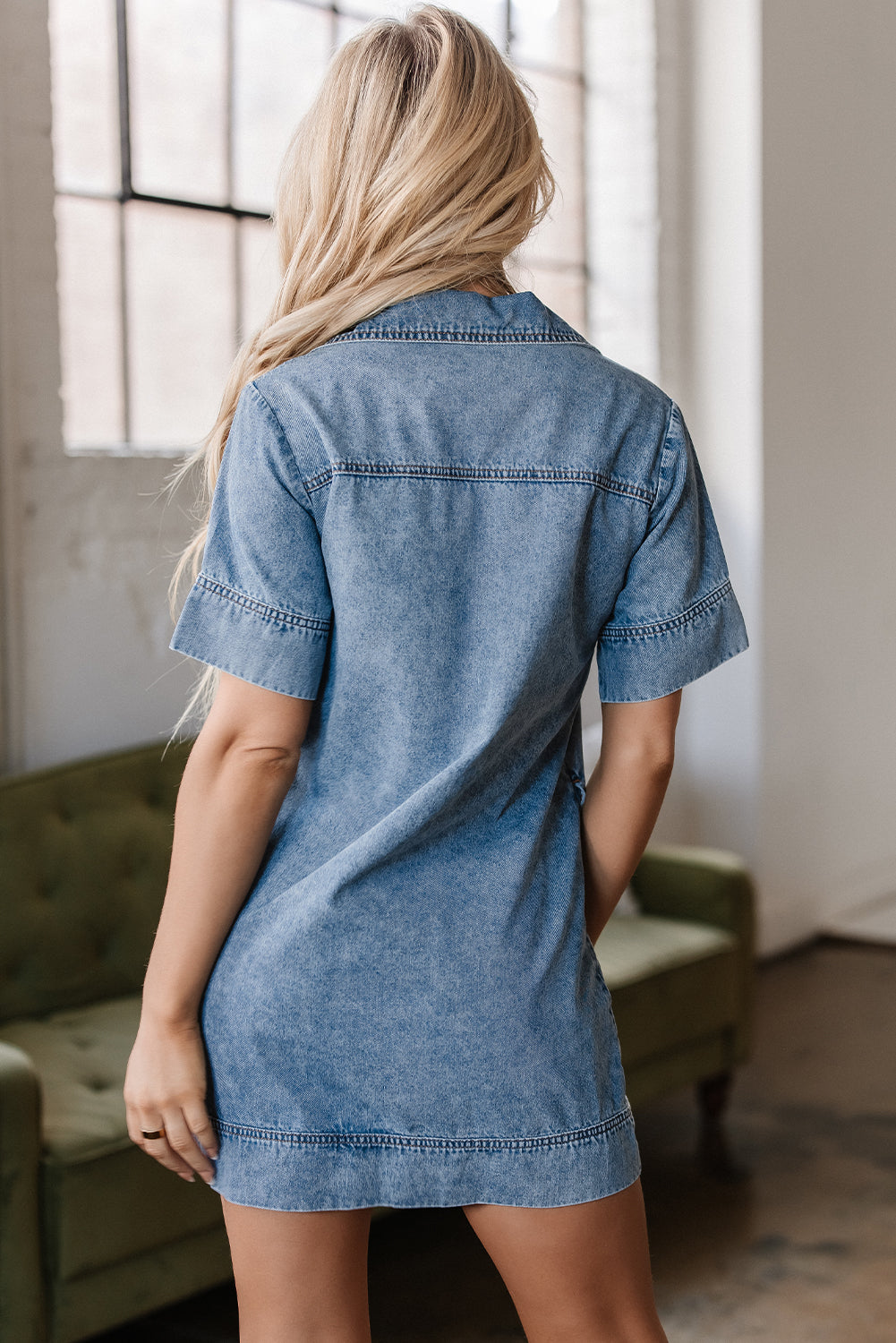 Woman wearing short sleeve denim dress, back view, in bright indoor setting