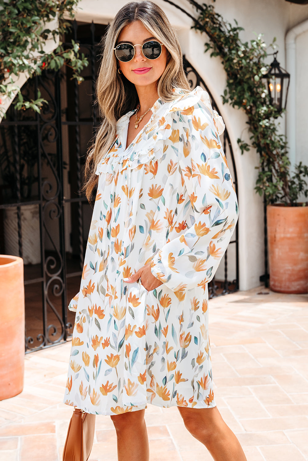 Woman in white floral long-sleeve dress with ruffle collar, sunglasses, outdoor setting