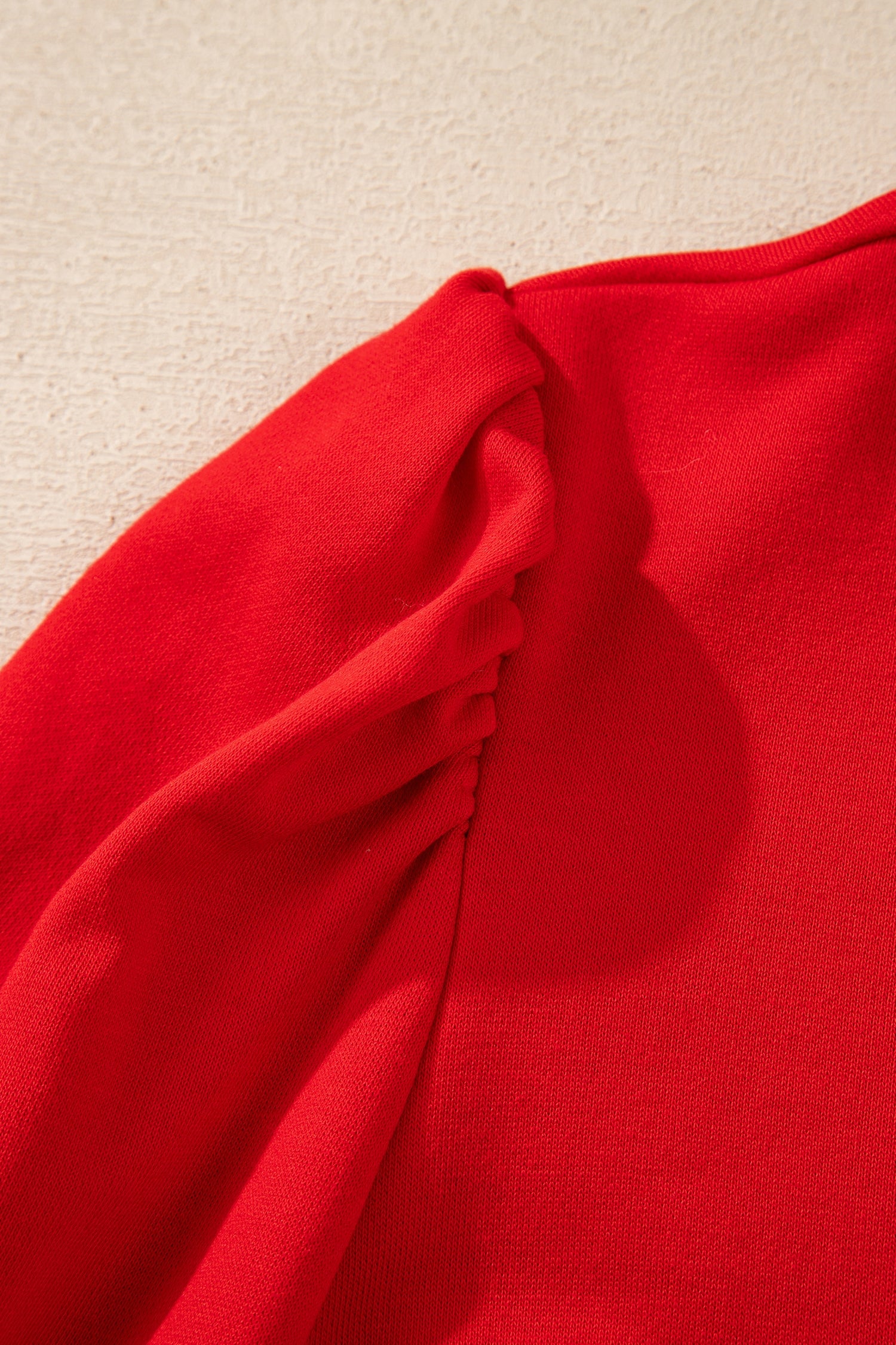 Close-up of red puff sleeve detail on textured fabric top