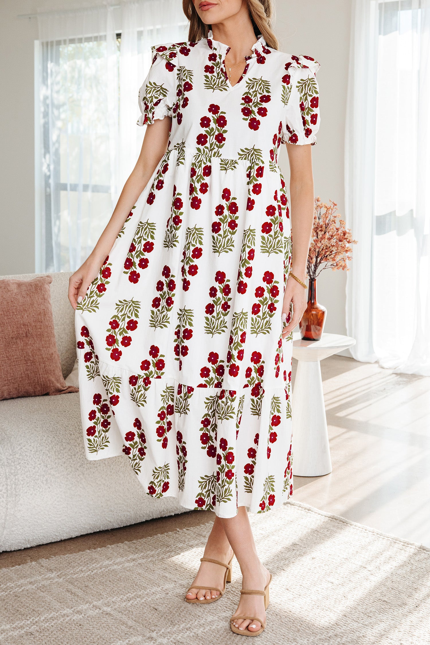 Woman wearing a white maxi dress with red floral print and puff sleeves in a bright living room