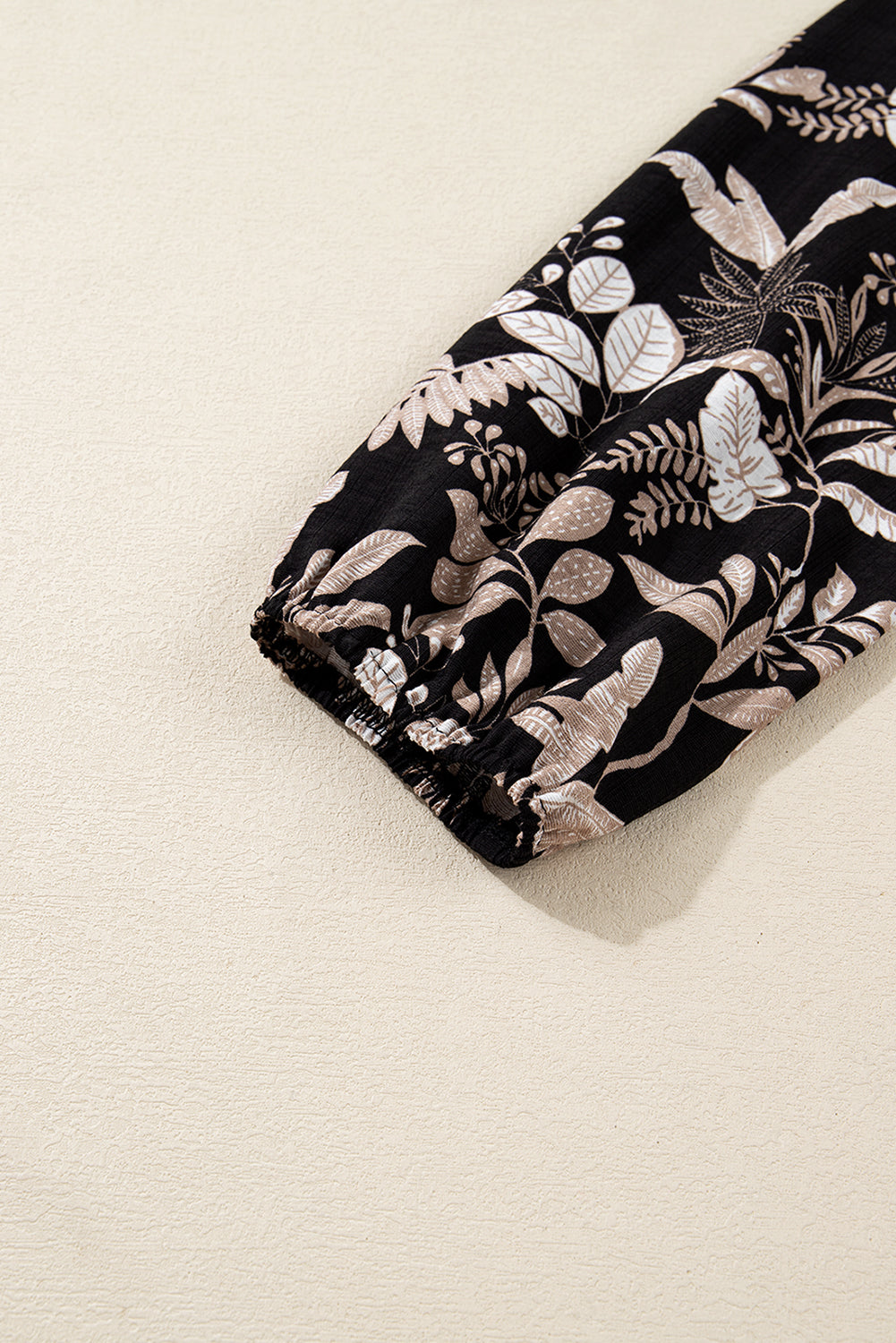 Black sleeve with beige botanical print and elastic cuff on neutral background