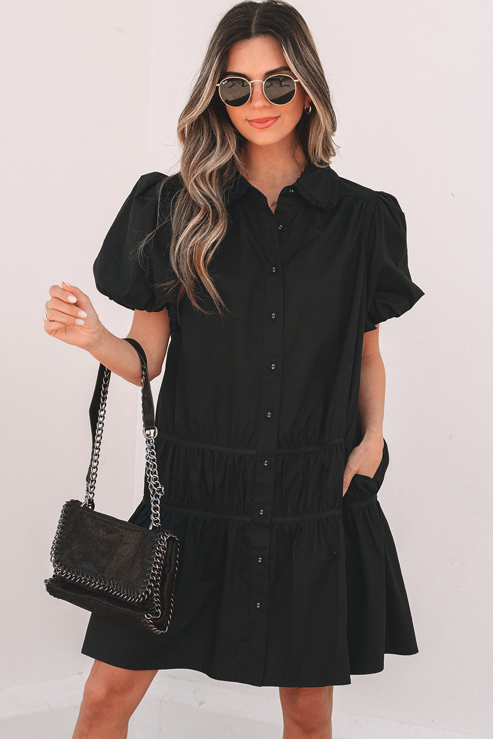 Woman wearing a black puff sleeve button-down dress, sunglasses, and holding a black chain bag