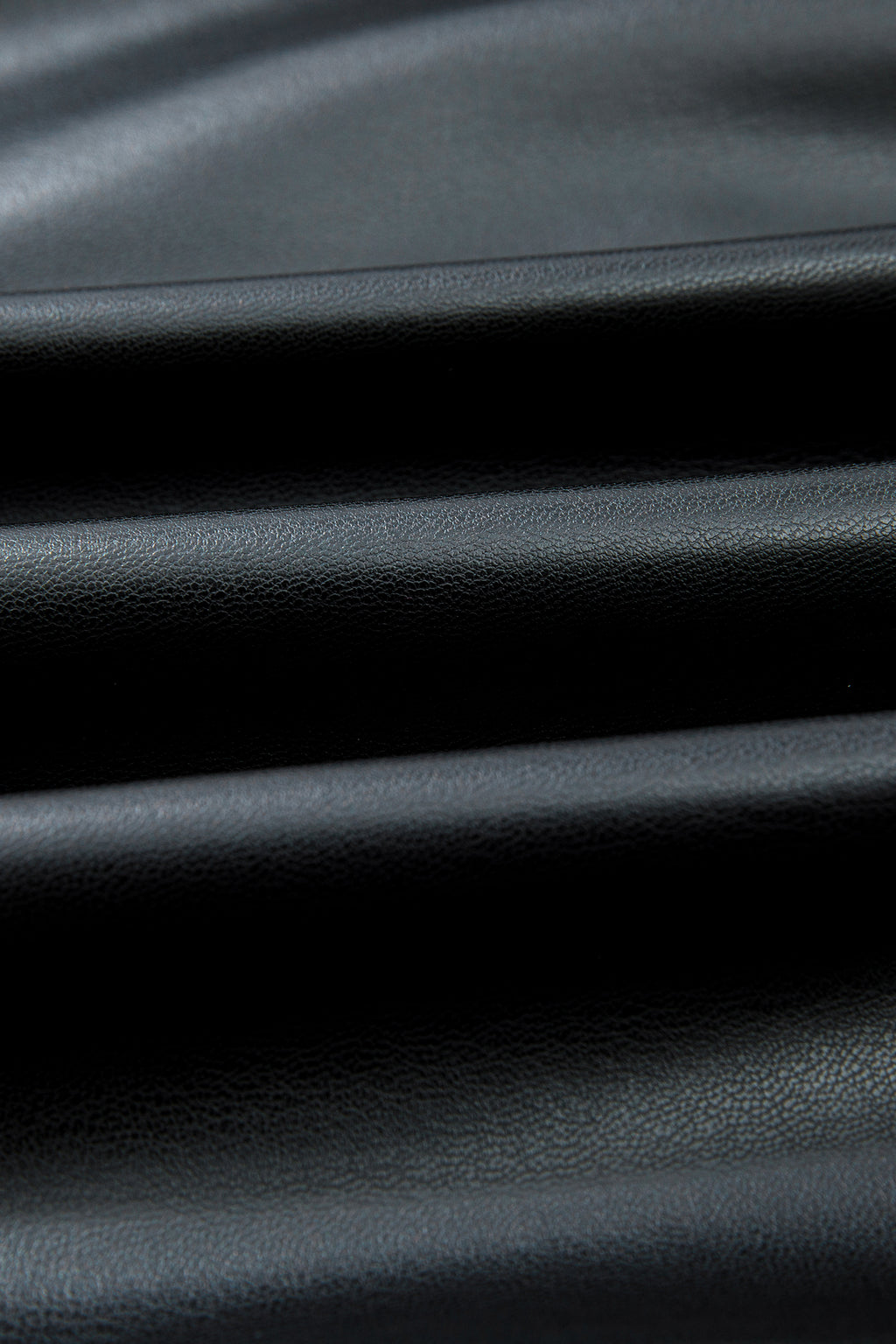 Close-up of black faux leather fabric with a smooth, textured surface and soft folds