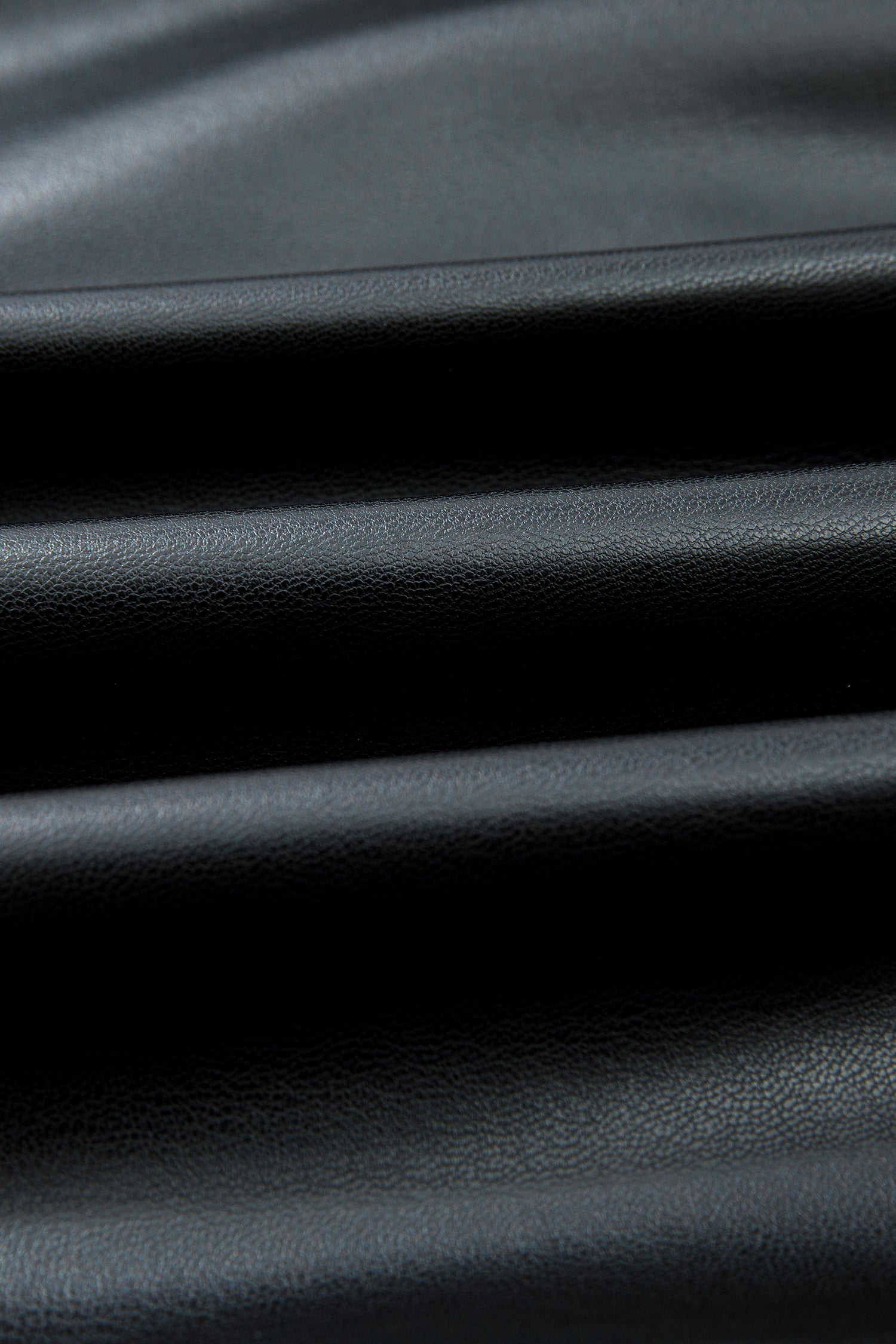 Close-up of black faux leather fabric with a smooth, textured surface and soft folds
