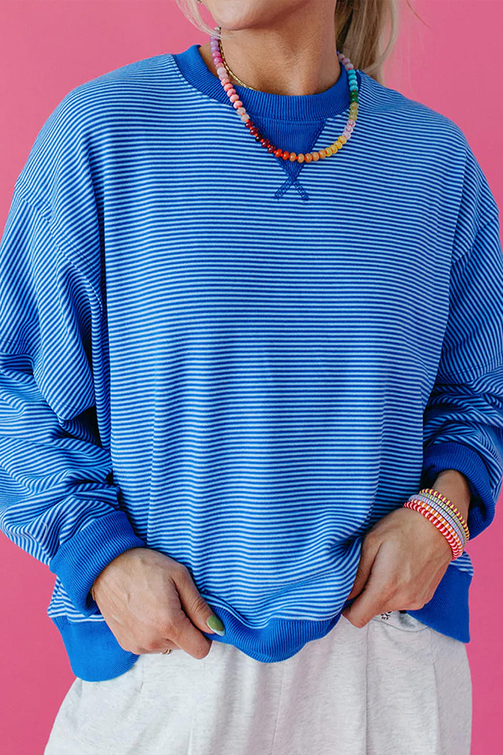 Синьо раиран oversized суичър с дълъг ръкав и рипсени маншети, заснет отпред върху розов фон