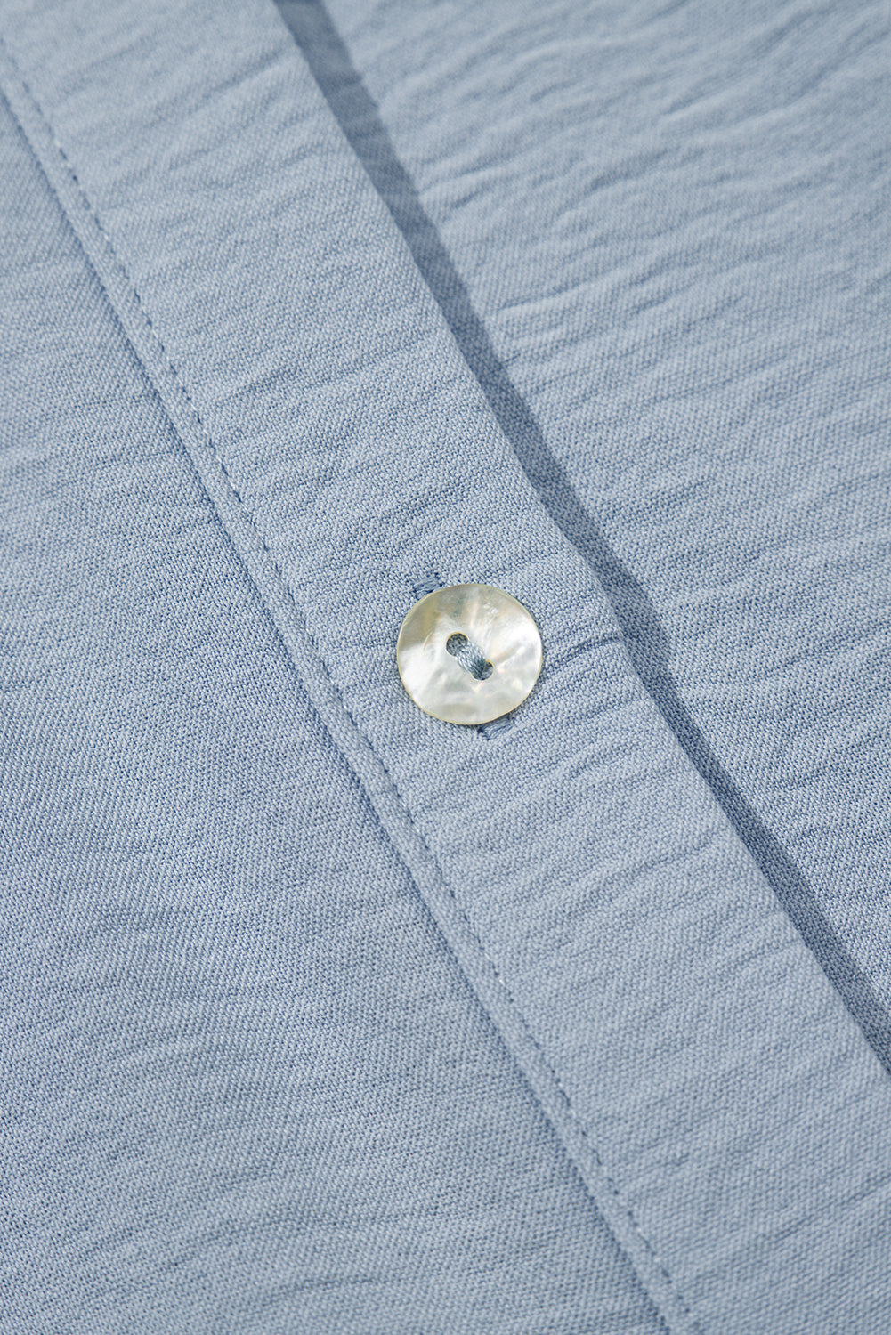 Close-up of light blue textured shirt fabric with a pearlescent button