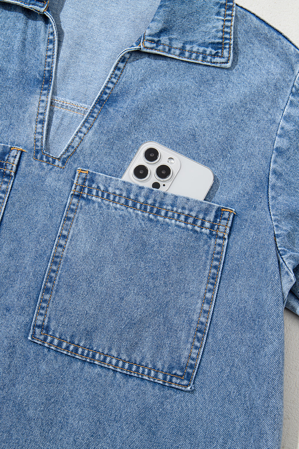 Light blue denim shirt with a chest pocket holding a smartphone