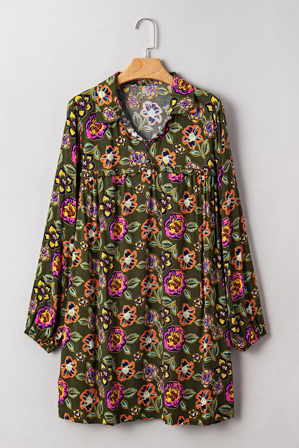 Long sleeve tunic with colorful floral print on dark green background, hanging on hanger