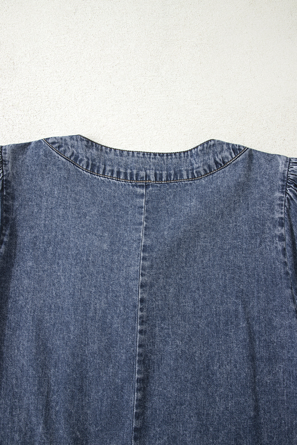 Close-up of denim dress back with seam detail and rounded neckline on light background
