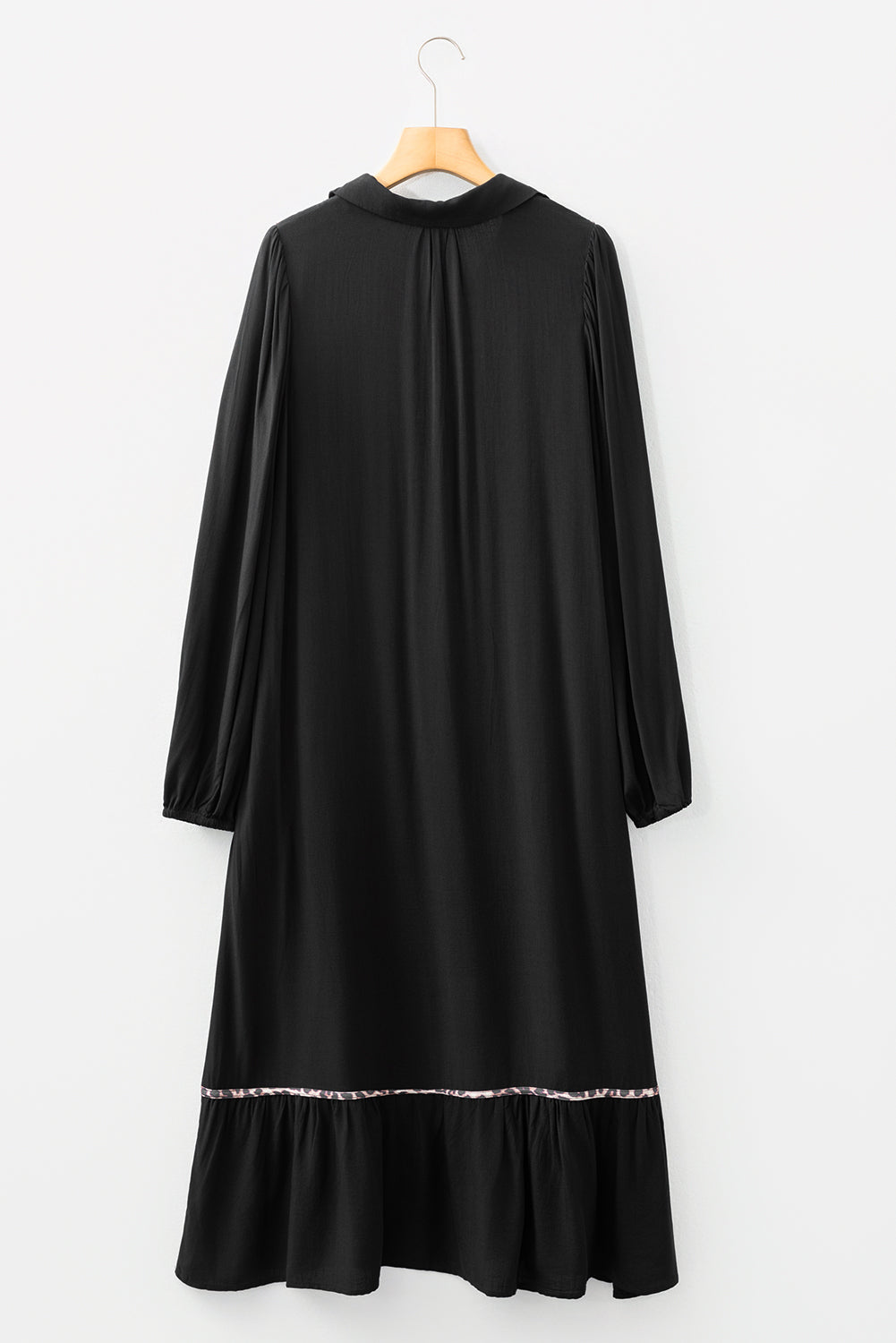 Black long-sleeve midi dress with ruffle hem and subtle decorative trim, hanging on hanger