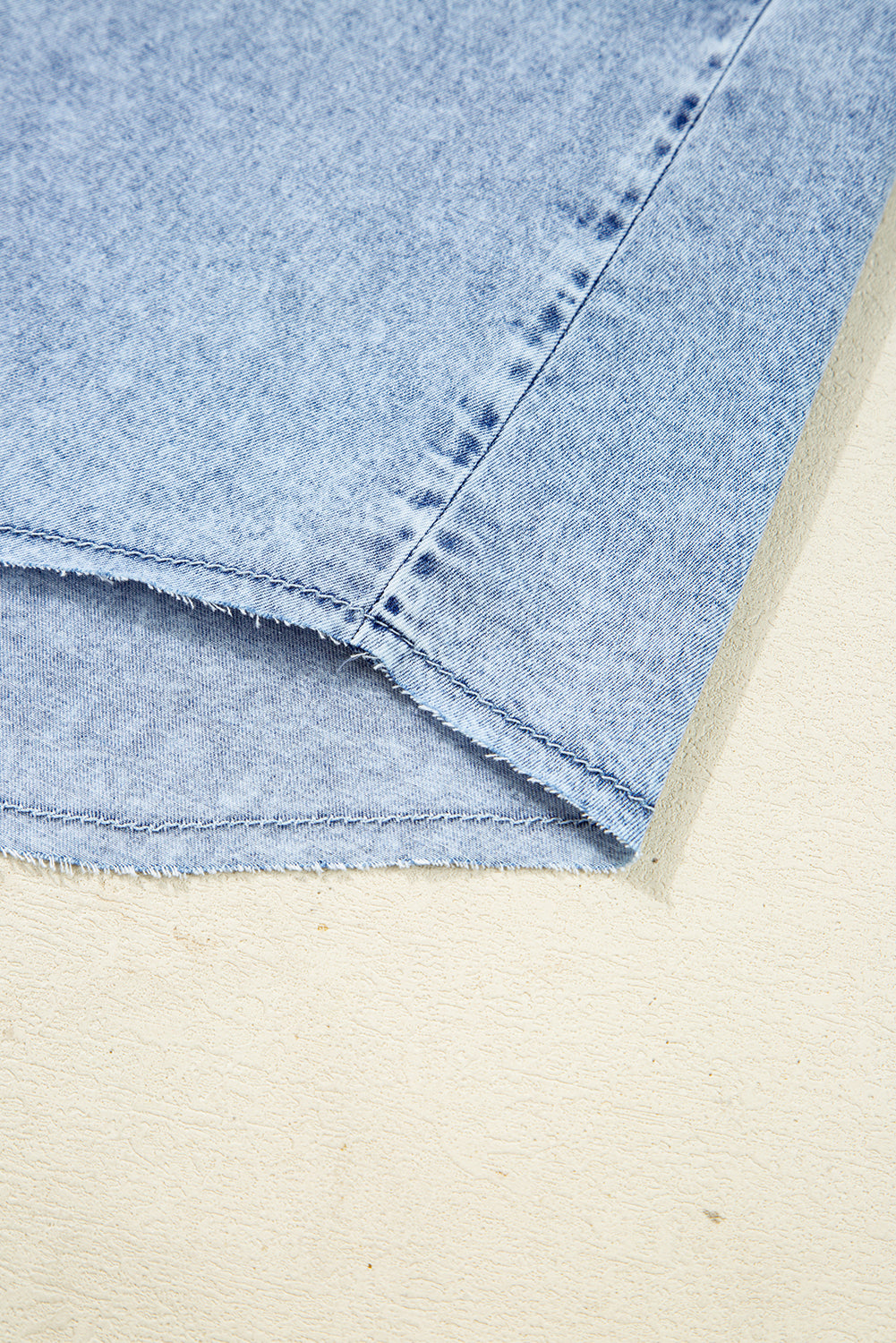 Close-up of light blue denim fabric with raw hem detailing on a neutral background