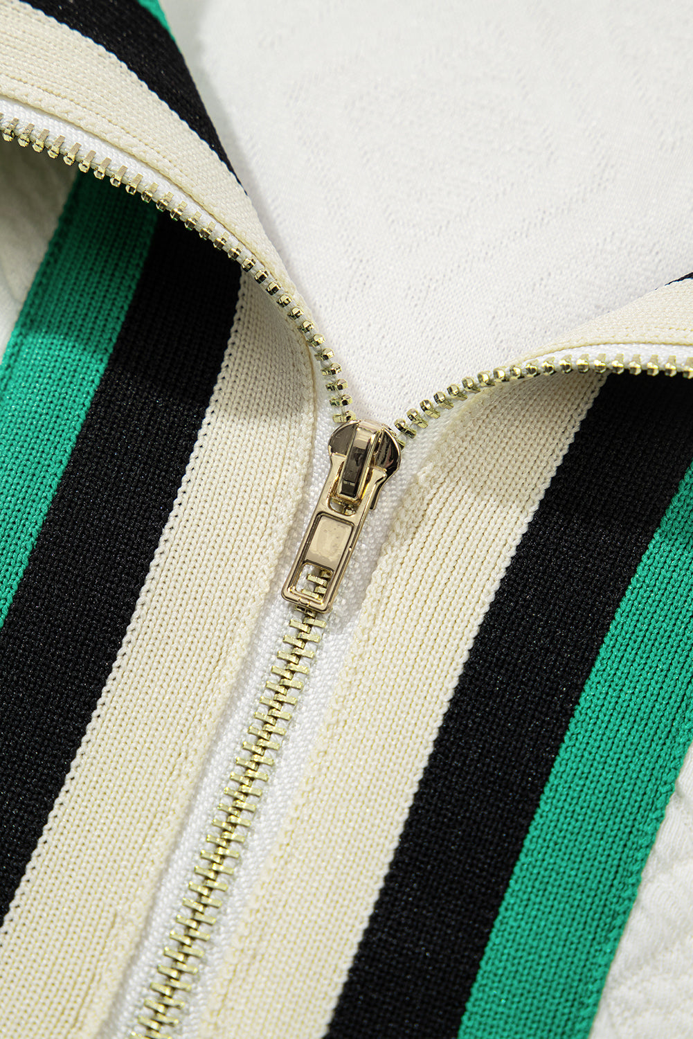 Close-up of gold zipper on knitted fabric with green, black, and cream stripes