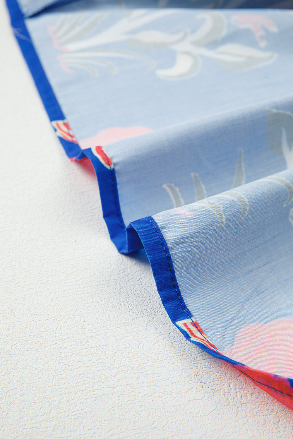 Close-up of light blue floral fabric with blue stitched edge, soft texture textile