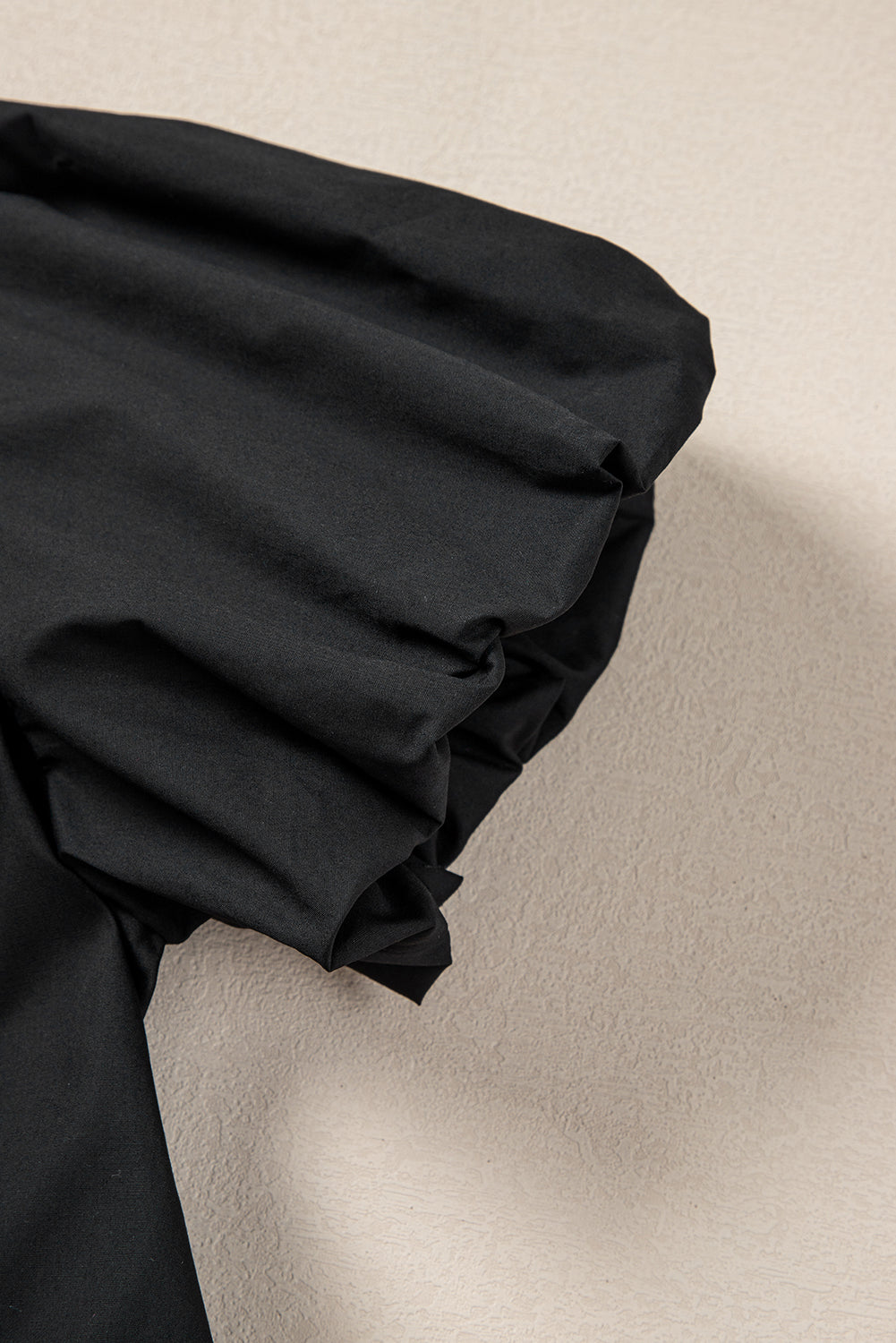 Close-up of a black puff sleeve on textured beige background, fashion detail