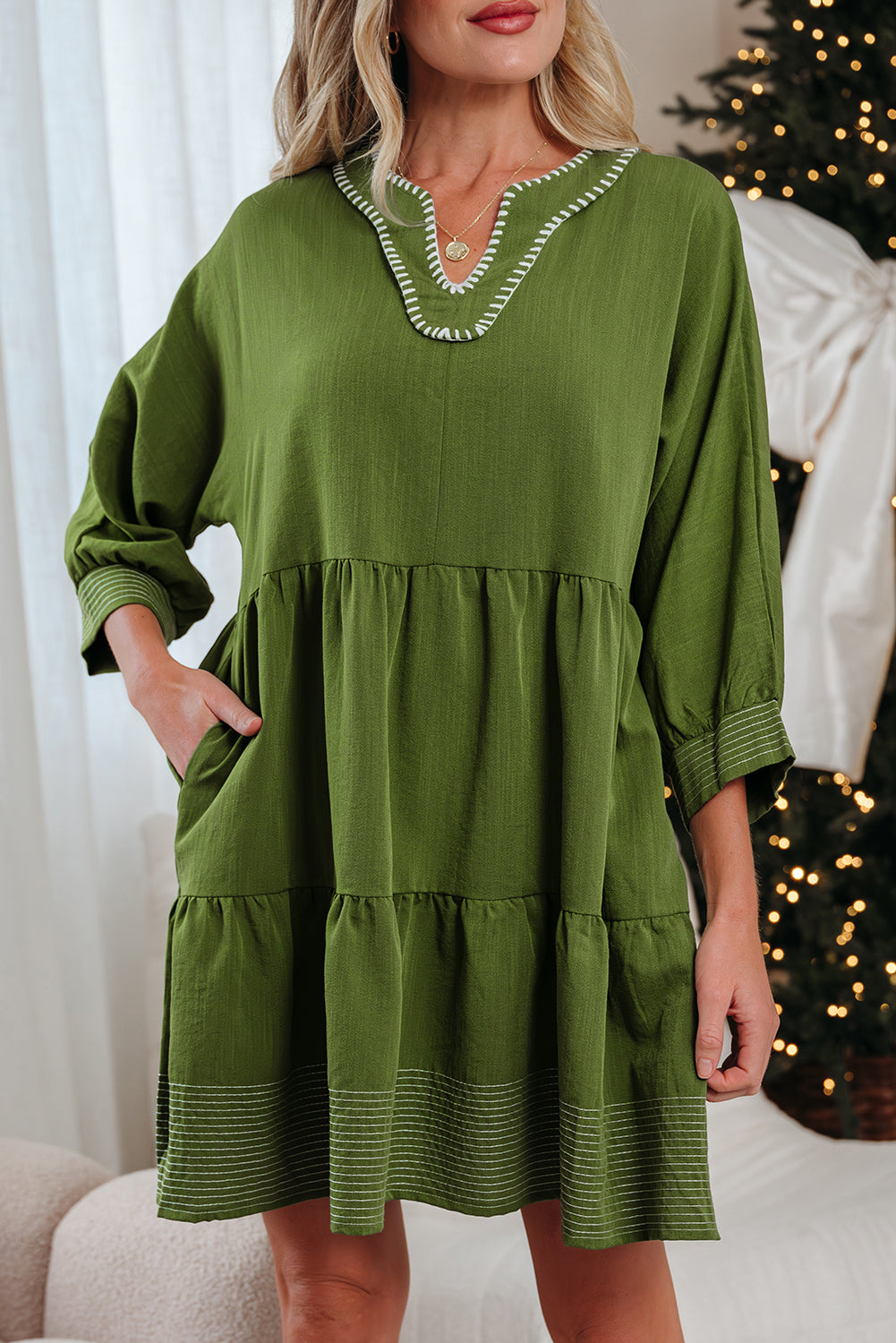 Woman wearing a loose-fit green tiered dress with white trim and long sleeves