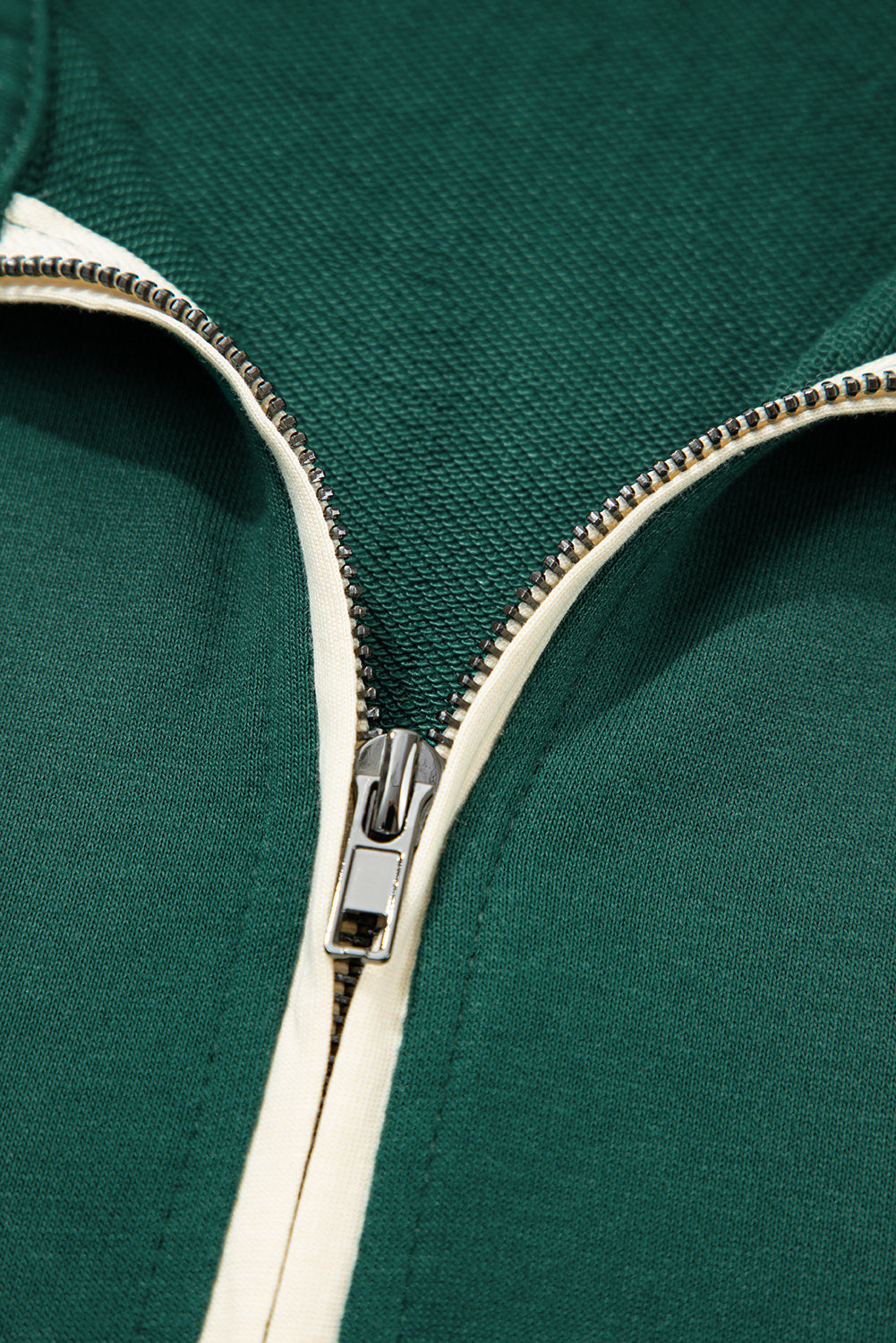 Close-up of green fabric zip-up jacket with silver zipper and cream trim