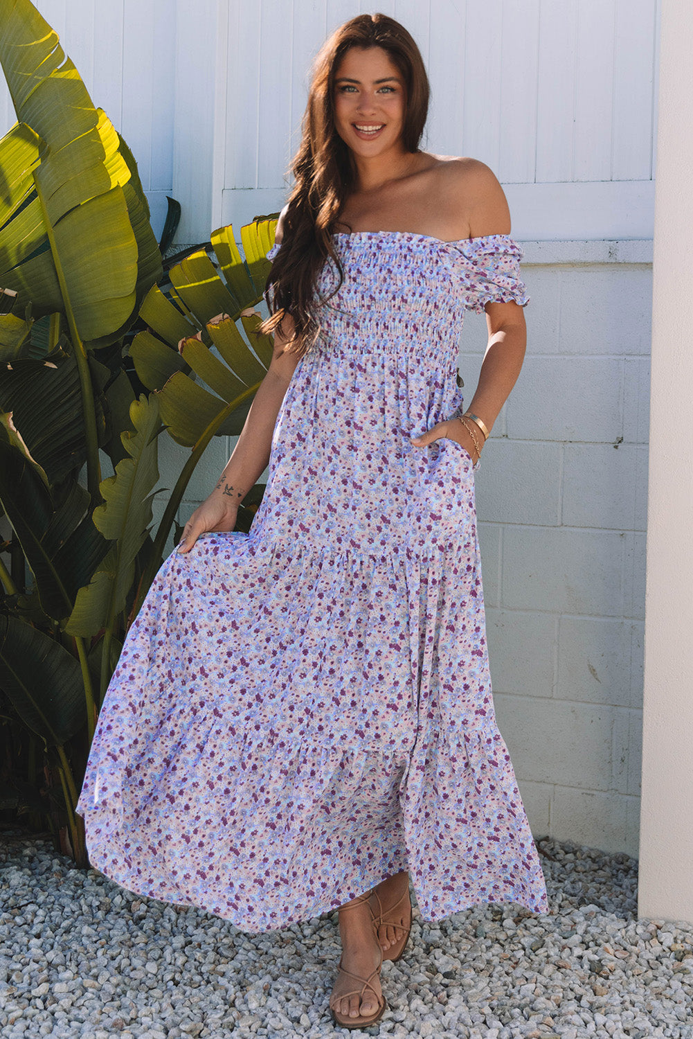 Woman in off-shoulder floral maxi dress standing outside near green plants