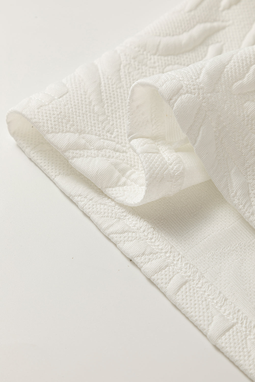 Close-up of textured white fabric with raised pattern and hemmed edge, home textile detail