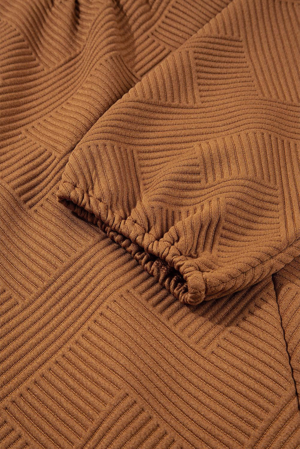 Close-up of brown ribbed knit fabric with geometric textured pattern and gathered sleeve cuff
