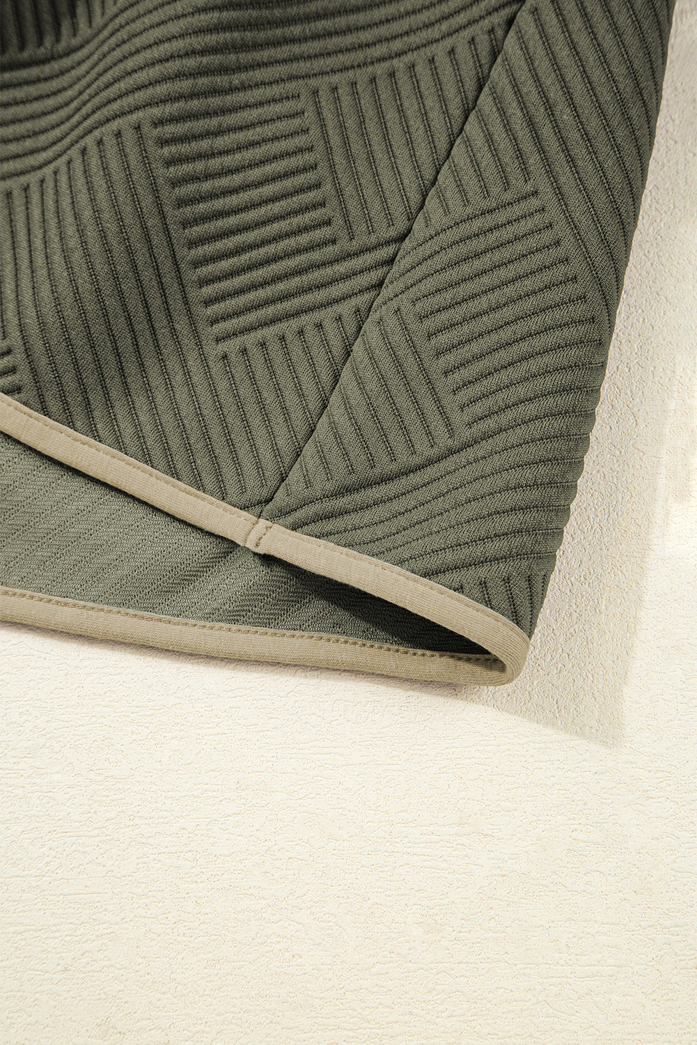 Close-up of textured green fabric with geometric ribbed pattern and beige trim