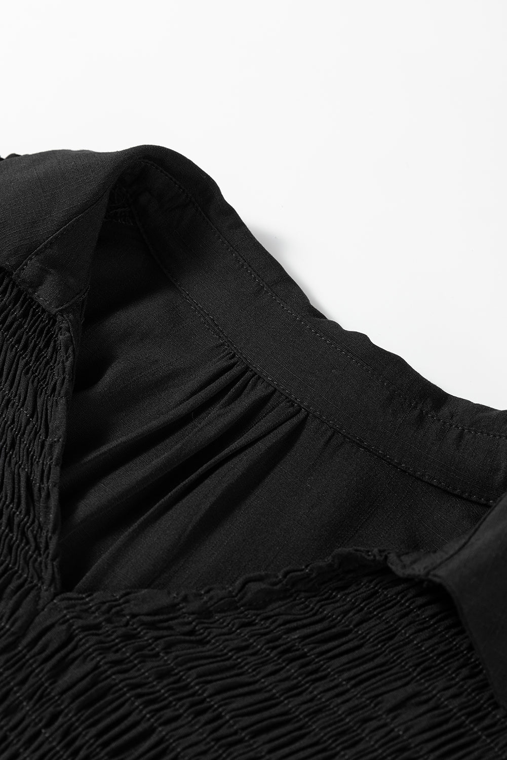 Close-up of black ruched fabric blouse with gathered neckline on white background