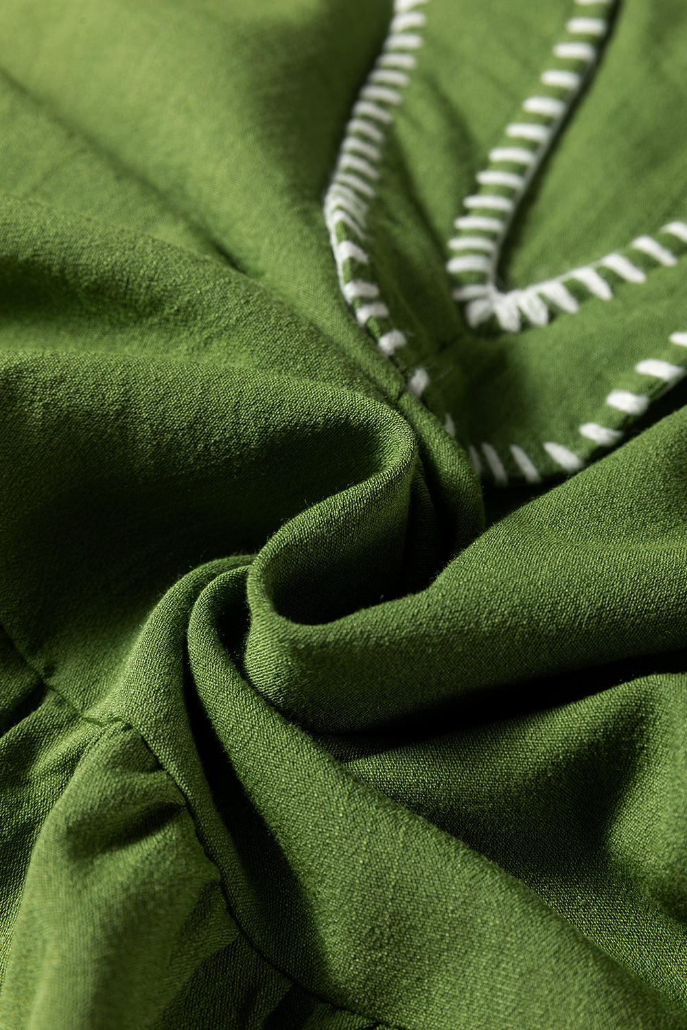 Close-up of green fabric with white stitching detail, soft texture textile material