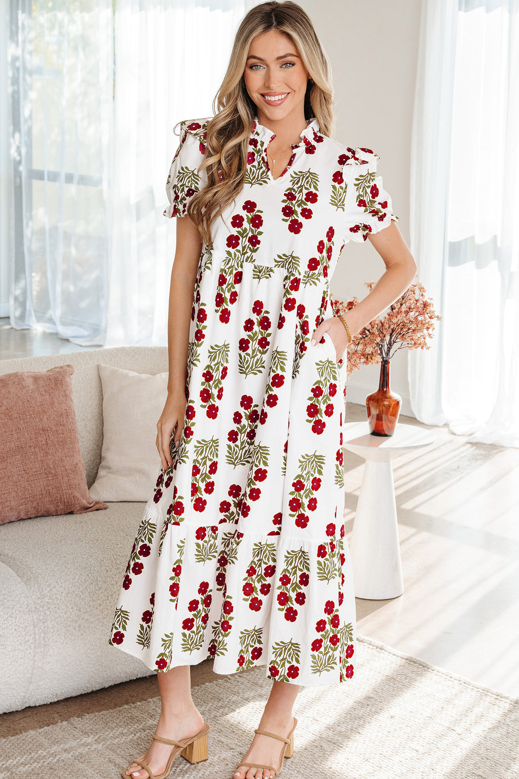 Woman wearing a white floral maxi dress with red and green flower print, standing indoors