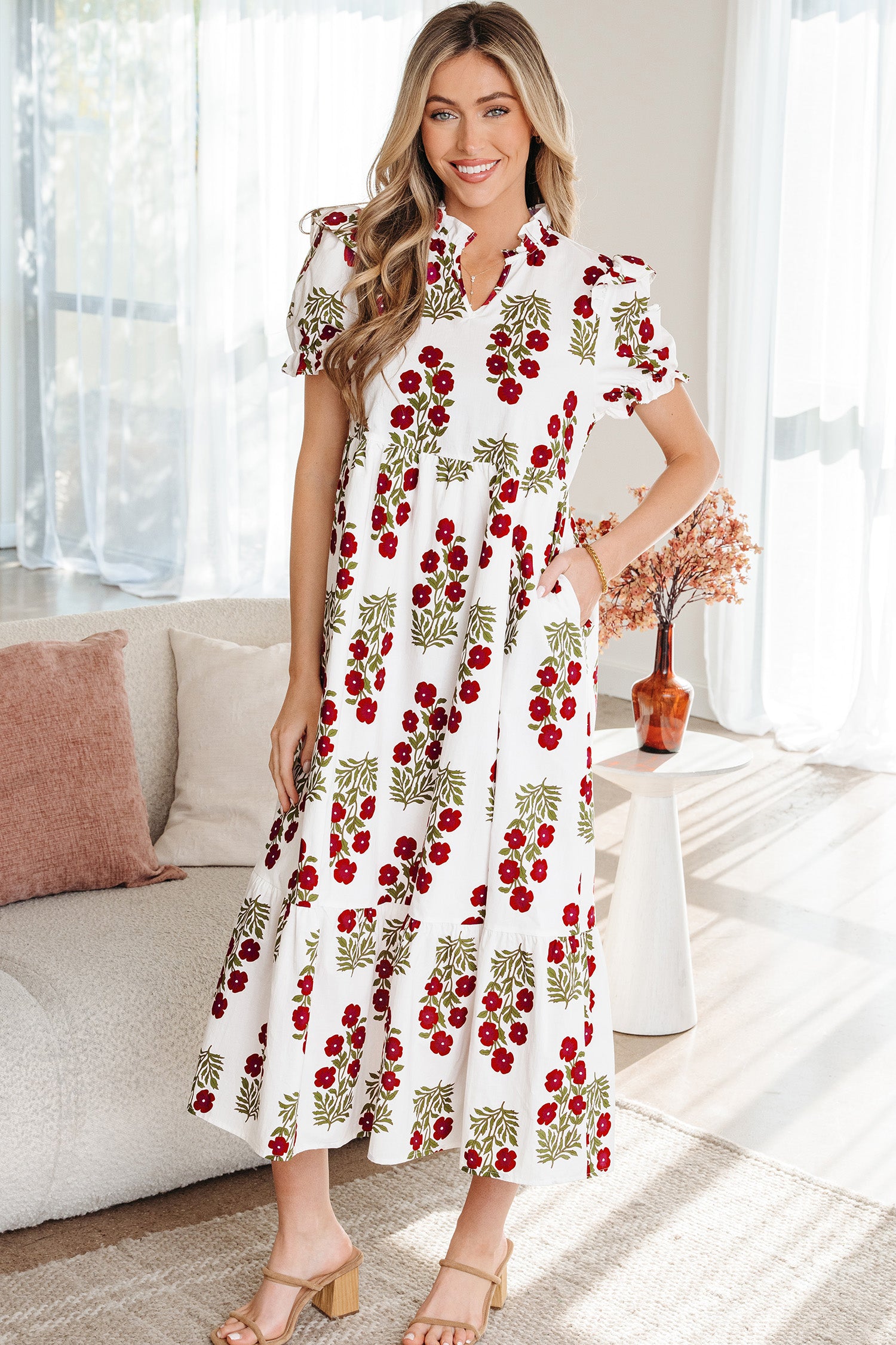 Woman wearing a white floral maxi dress with red and green flower print, standing indoors