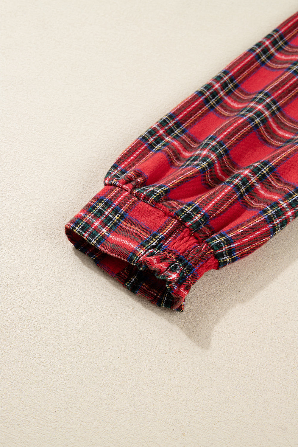 Close-up of red plaid flannel sleeve with elastic cuff on neutral background
