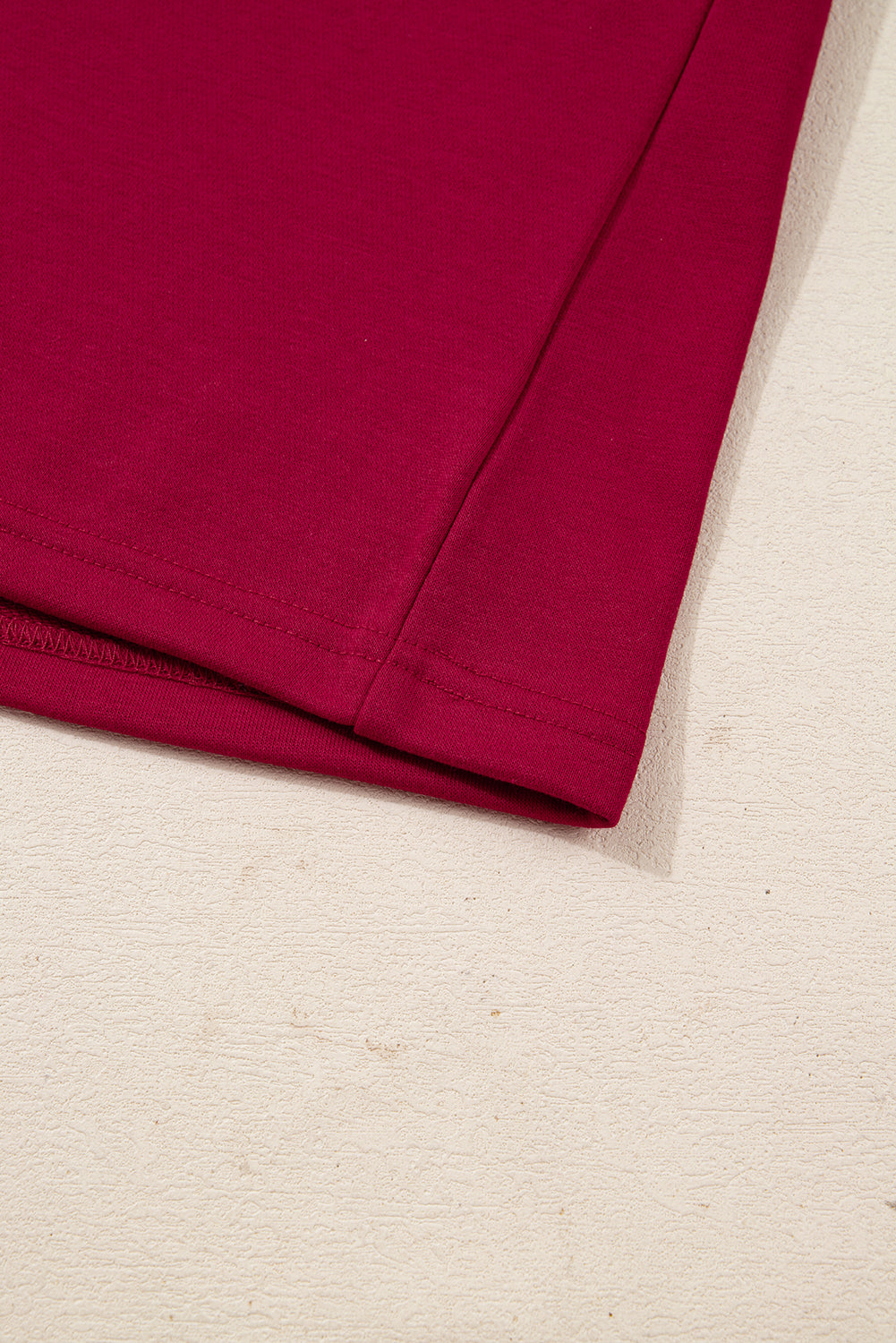 Close-up of red cotton t-shirt hem on light textured surface