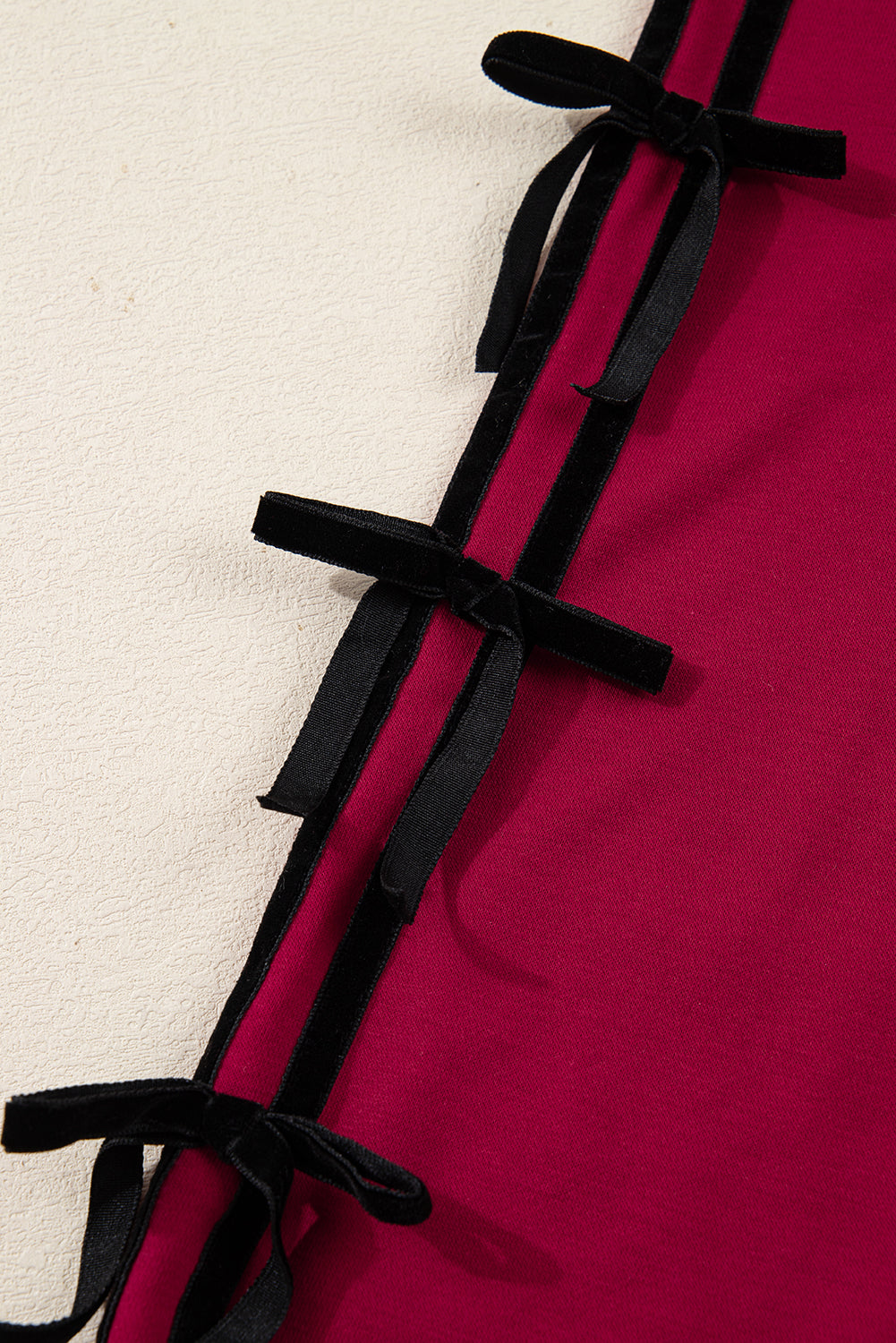 Close-up of red fabric with black velvet ribbon bows, textured background