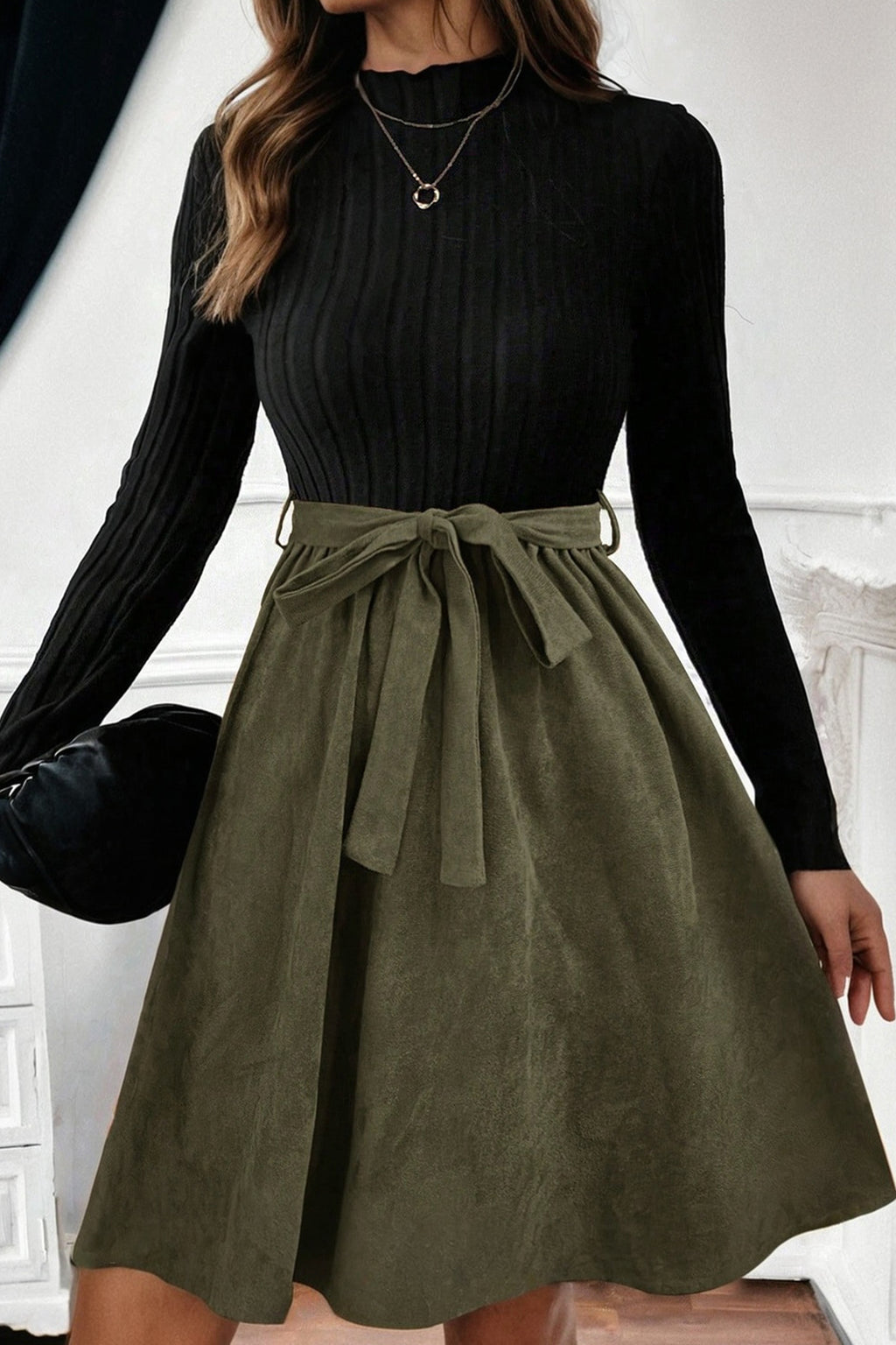 Woman wearing long sleeve black ribbed top and olive green belted midi skirt dress