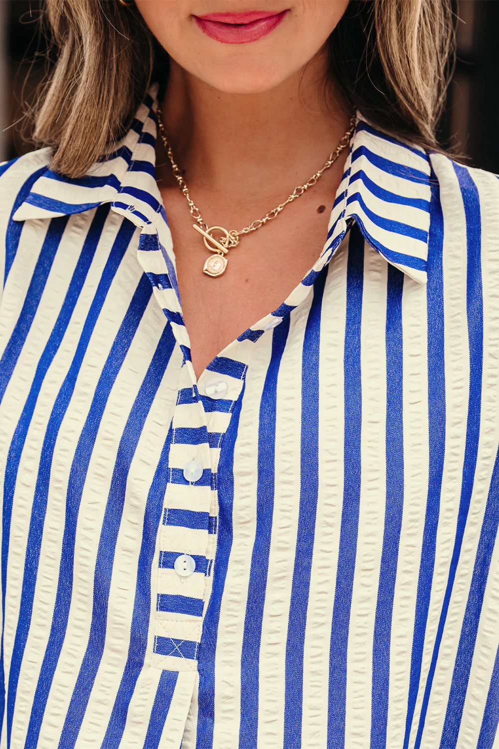 Woman wearing blue and white striped shirt with gold chain necklace