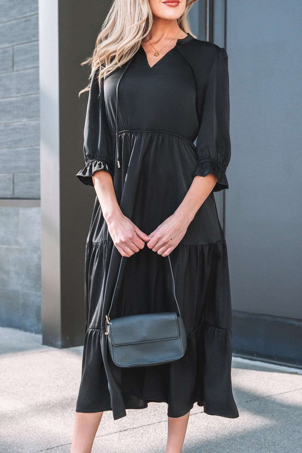 Woman wearing a black midi dress with ruffle sleeves, holding a black shoulder bag