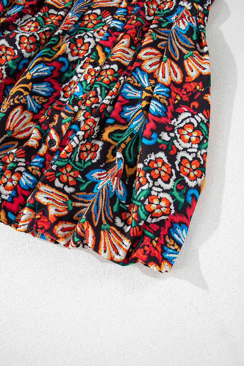 Colorful floral print dress fabric with pleats and button details on a white background