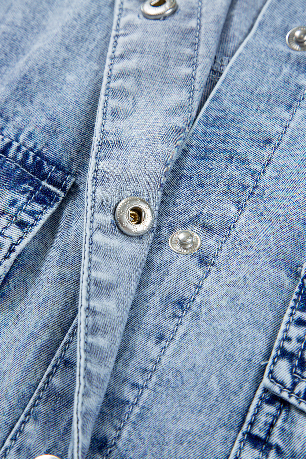 Close-up of light blue denim fabric with metal snap buttons and visible stitching