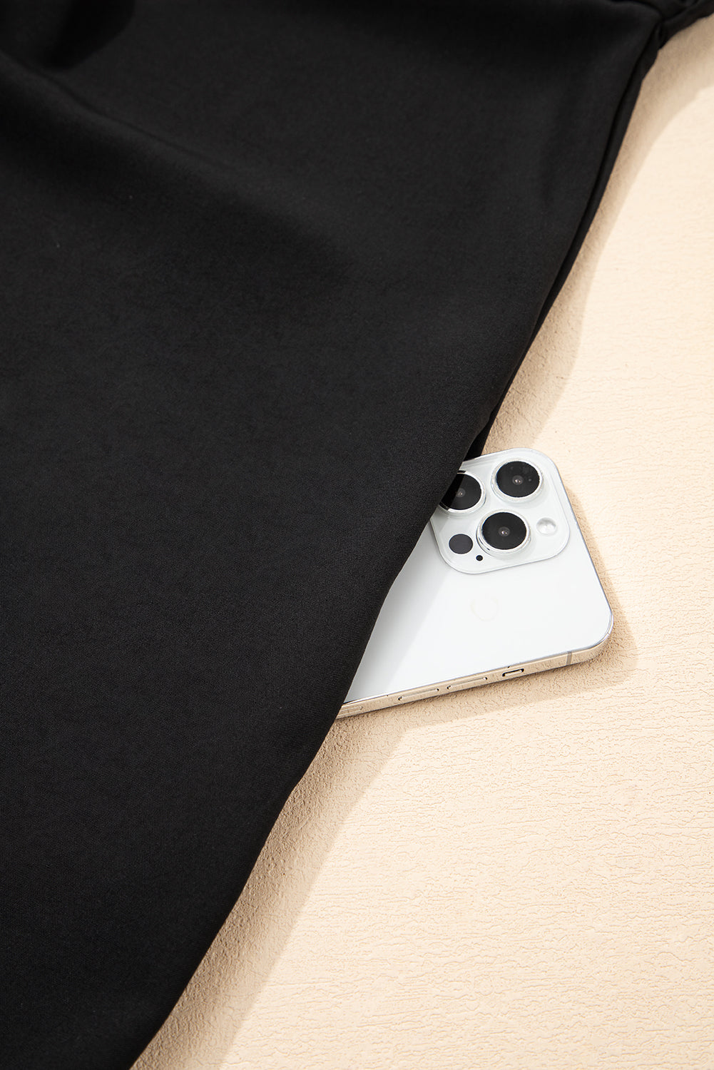 Black clothing pocket with smartphone partially inside on beige surface