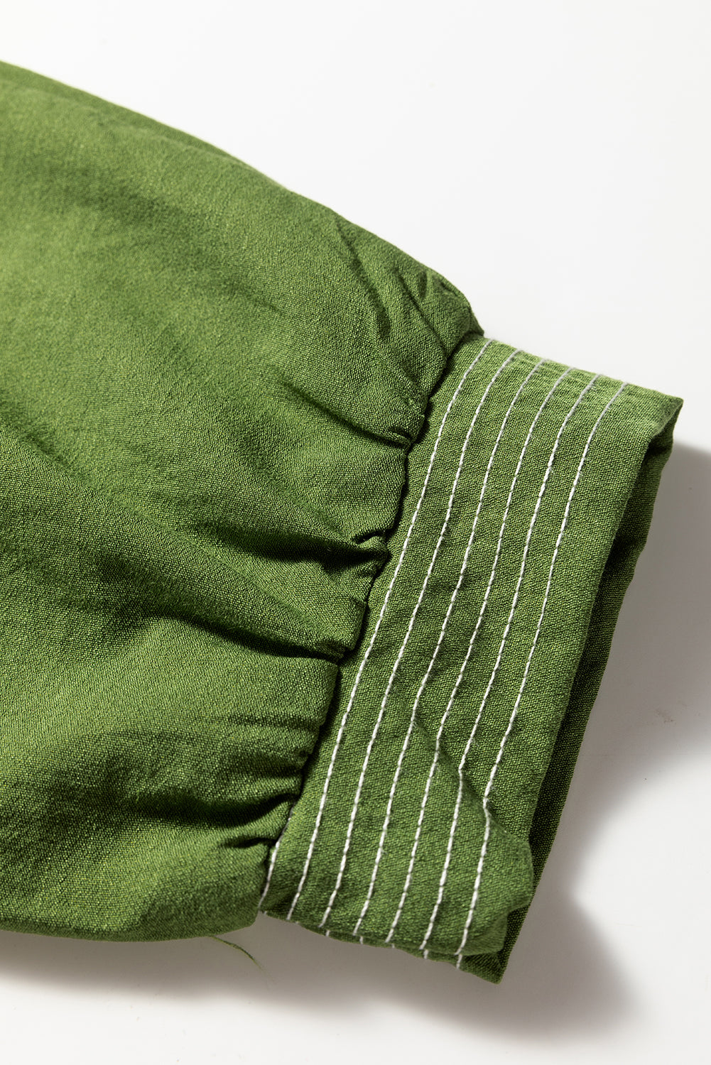 Green fabric sleeve with gathered cuff and white stitched detail