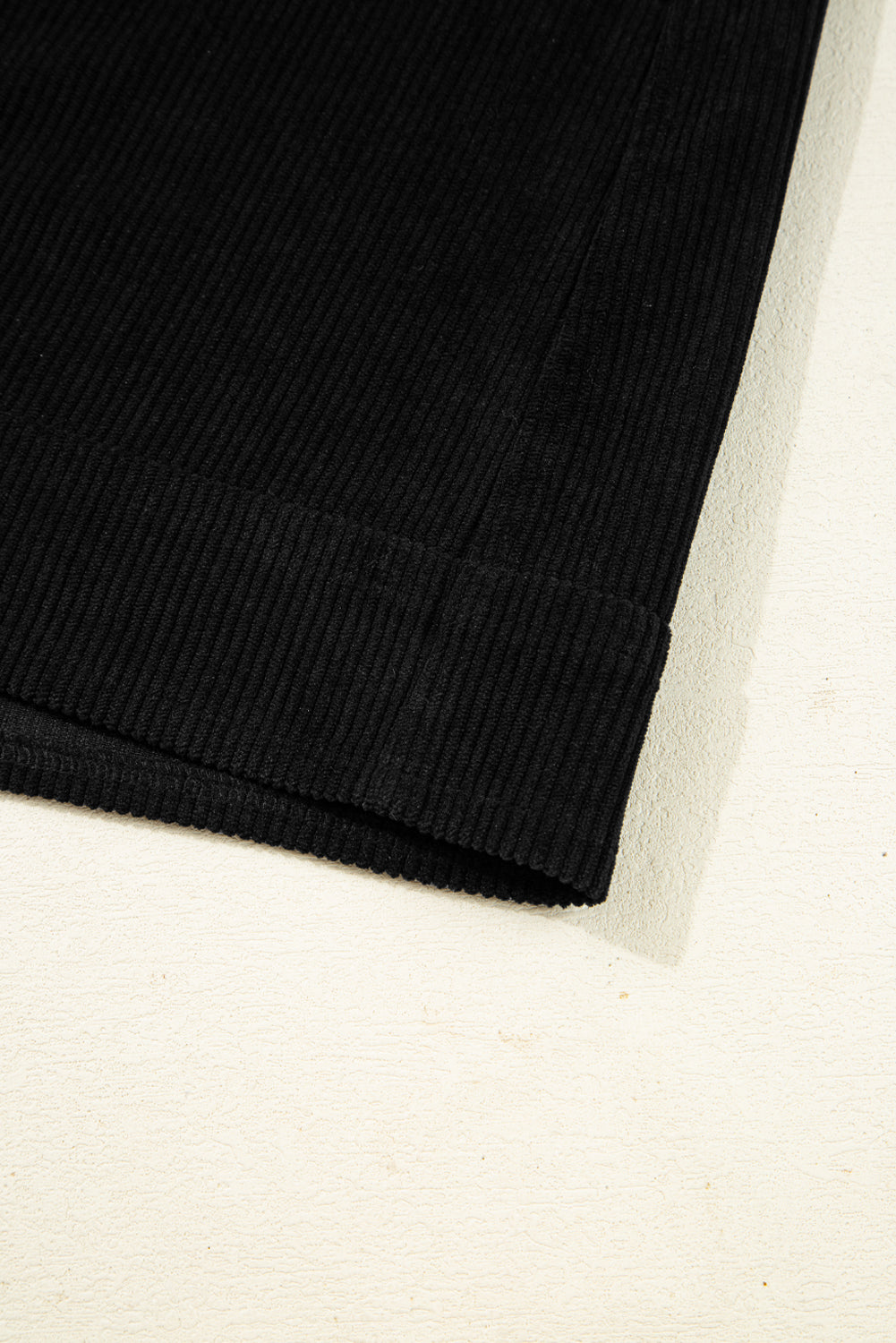 Close-up of black ribbed knit fabric with folded hem, clothing textile detail