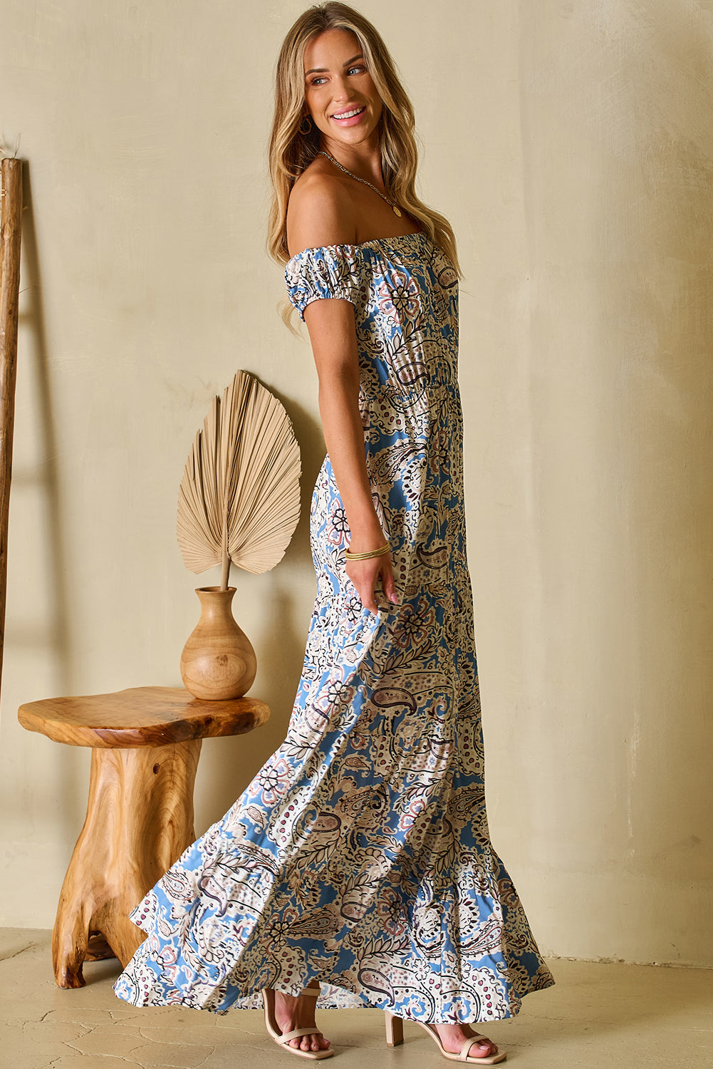 Woman wearing off-shoulder boho maxi dress with blue paisley print, standing indoors