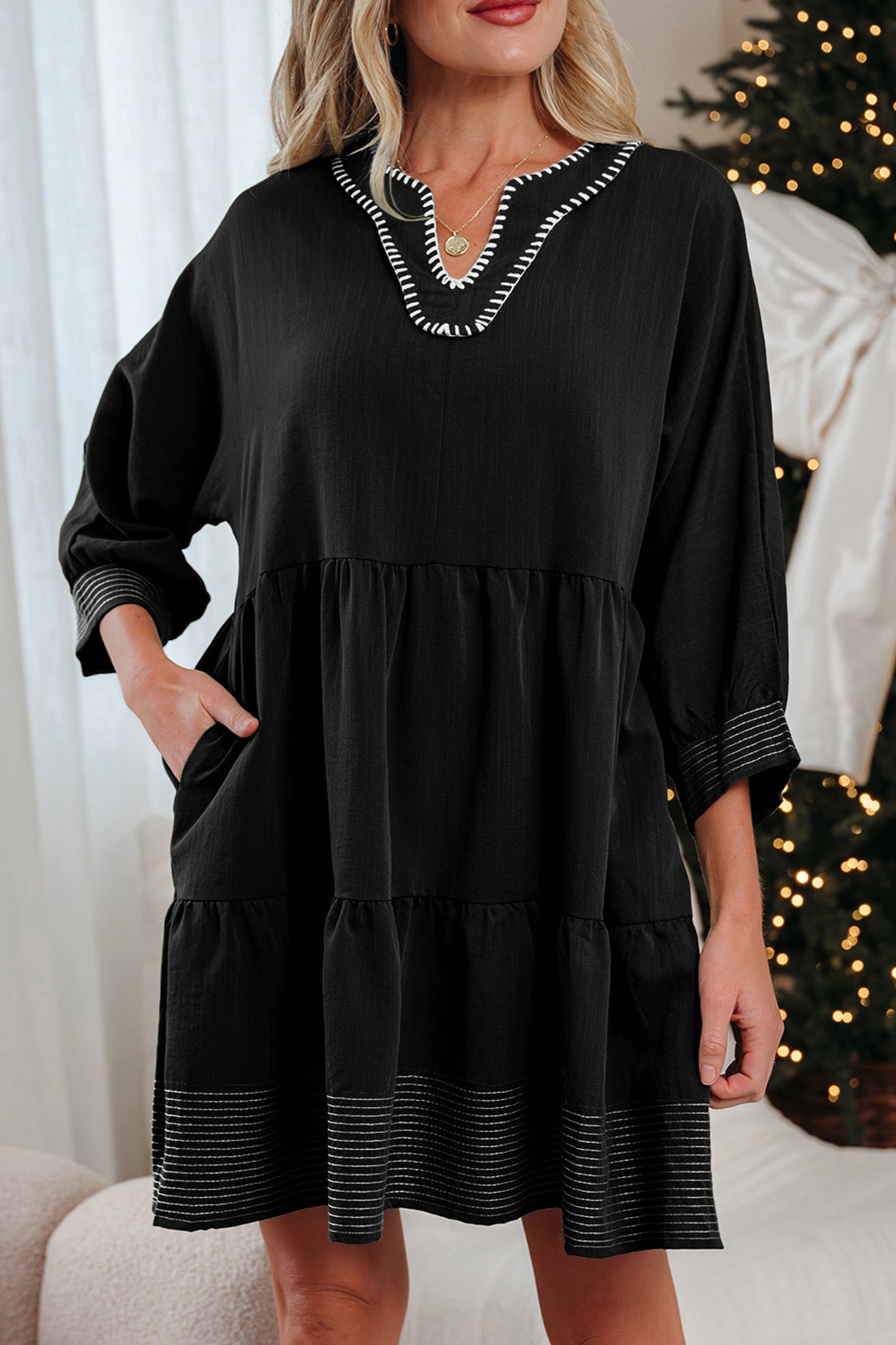 Woman wearing a black long sleeve tiered dress with white trim, holiday decor in background