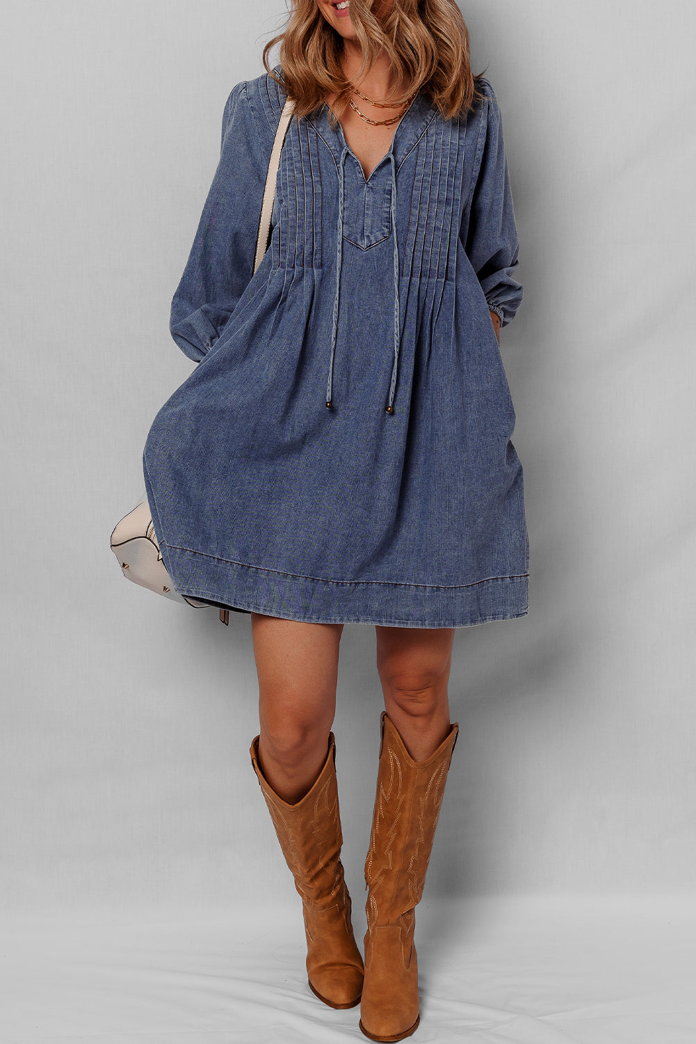 Woman wearing a casual denim mini dress with long sleeves and tan cowboy boots