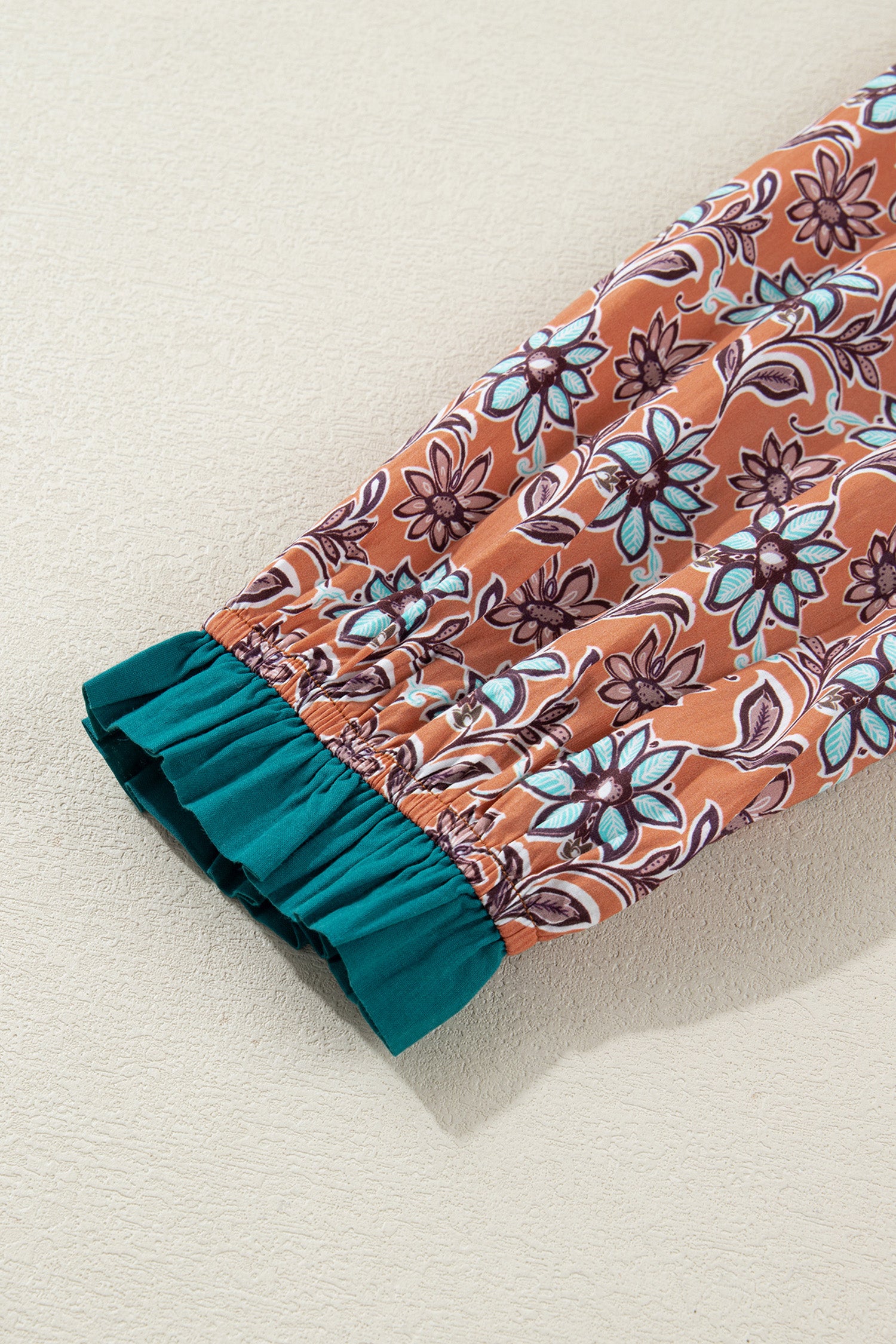 Floral patterned sleeve with elastic teal cuff on textured surface